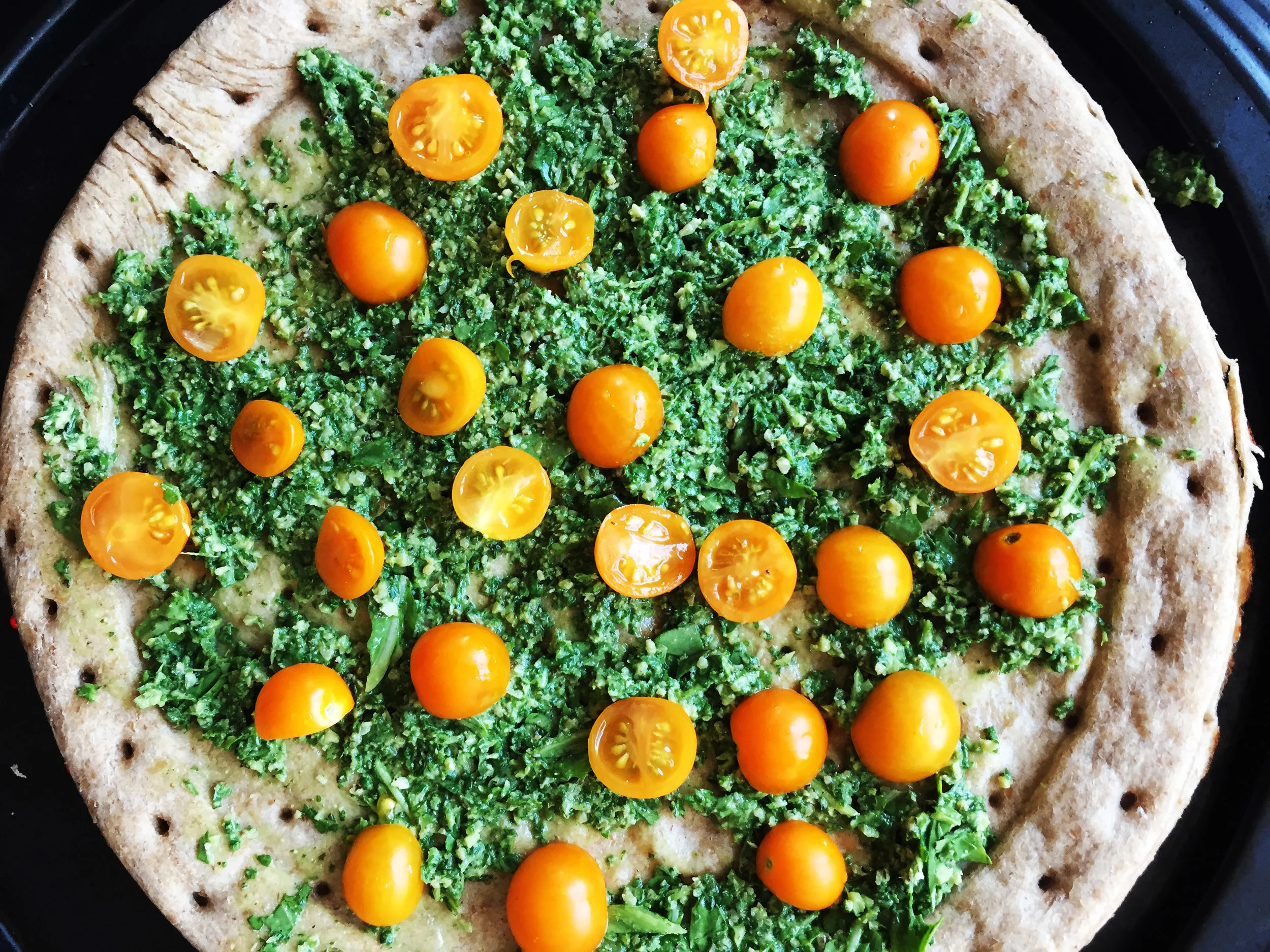 6. While potatoes and tempeh continue to cook, add the halved tomatoes to the pizza crust as seen above. We want a nice healthy layer of tomoatoes.