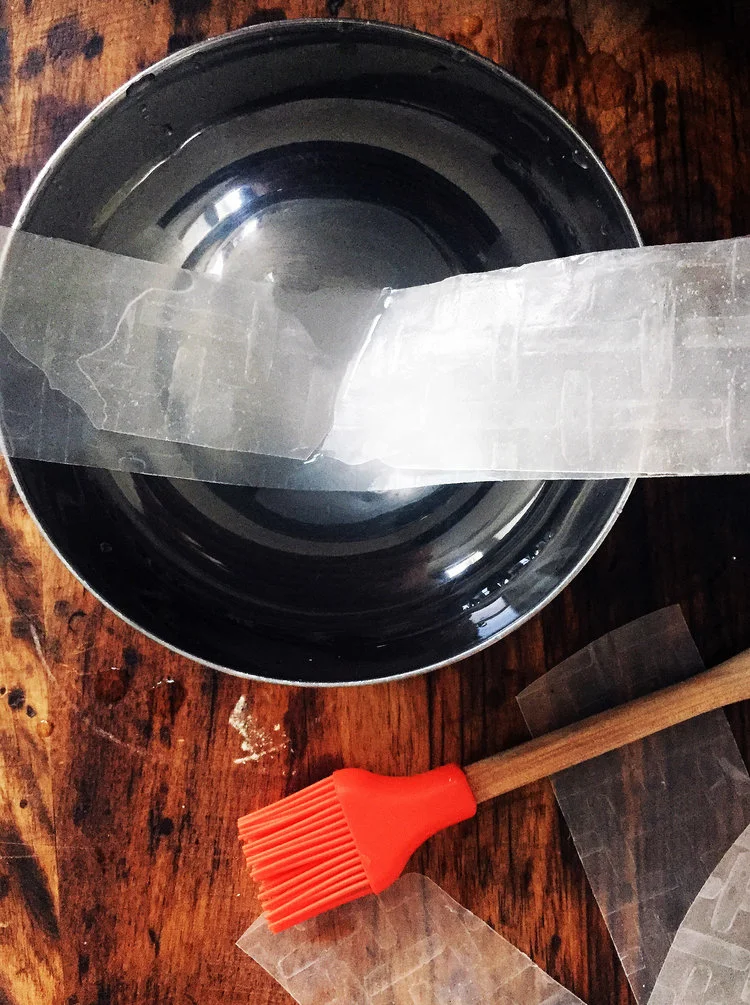 3. To form, the bacon pieces, take two strips of rice paper and stack them on top of each other, dunk the ends into the water, then the middle, and smash them together. Run your fingers down the paper to remove excess water.