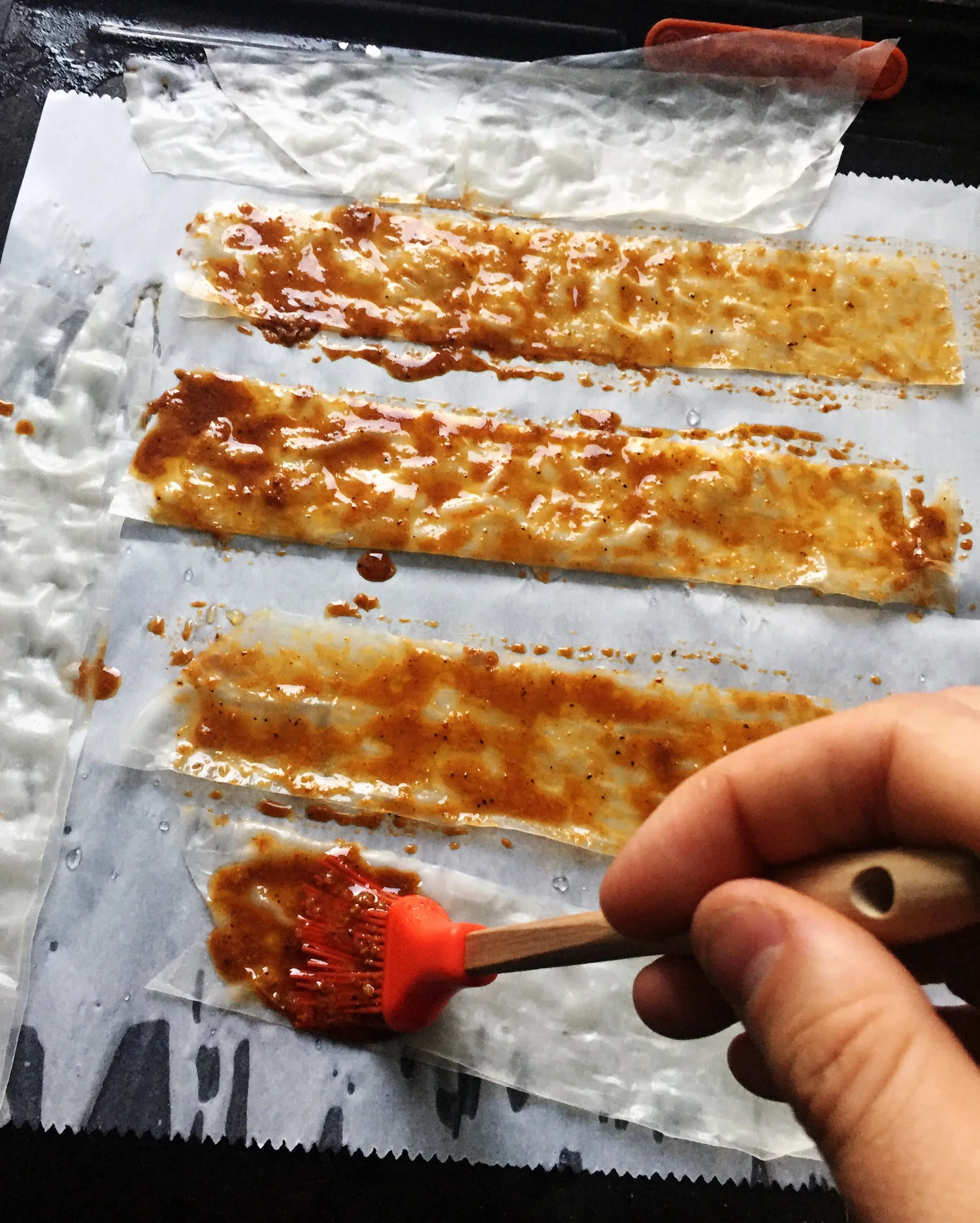 5. Using a pastry brush, slap on the marinade onto each strip. Coat well. Flip over the strips and add the marinade to the other side. Place the pans of bacon into the oven and bake at 400F for 8-9 minutes. At 6-7 minutes check it to make sure it is not burned. I keep a close eye as it can burn quickly.
