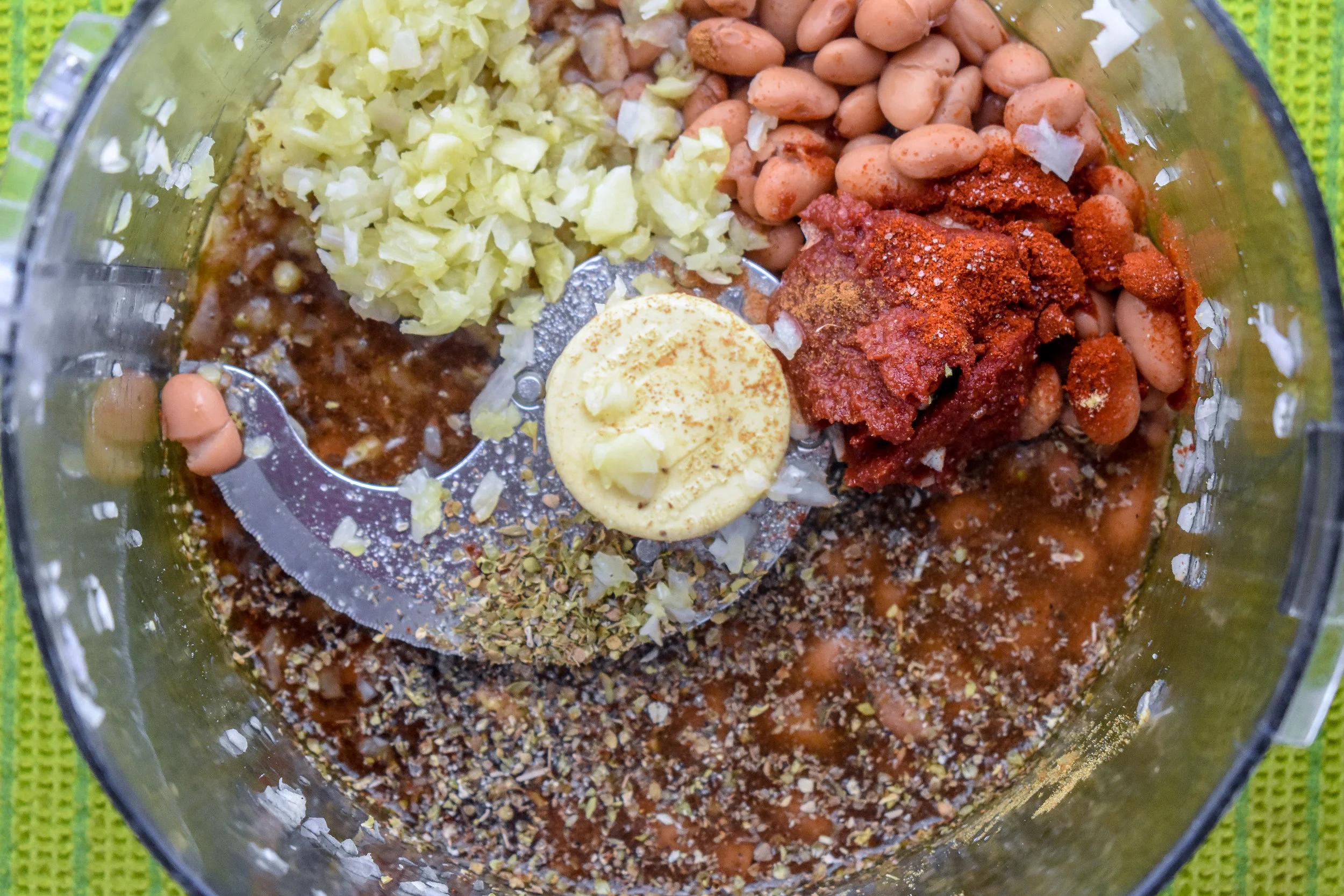 2. Add onions + garlic to food processor or high-speed blender along with beans, water, coconut aminos, tomato paste, and spices. Mix until it creates a smooth paste.