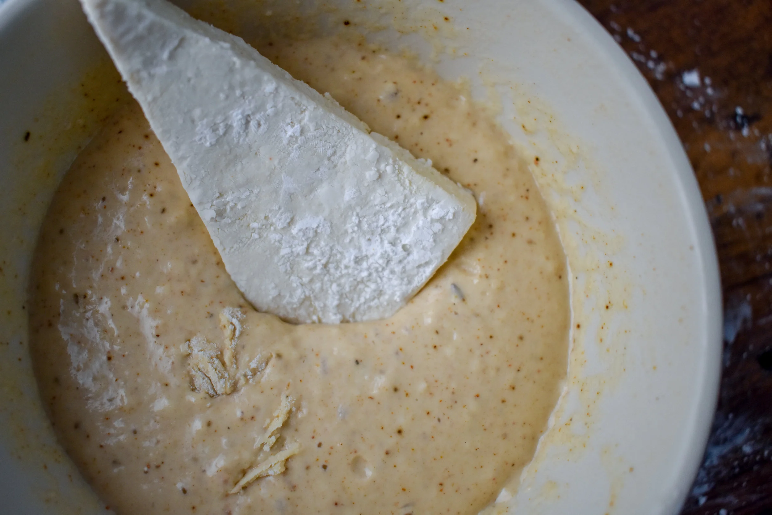 7. Next, place 1/4 cup canola or safflower oil in a deep pot or pan over medium-high heat. Get the oil to 180F. Warm for about five minutes. Once the oil is warmed, test by dropping a tiny piece of bread in the oil. If it floats at the top, you’re ready. Take each piece of tofu and place into the batter, coat fully, and drop into the pot.