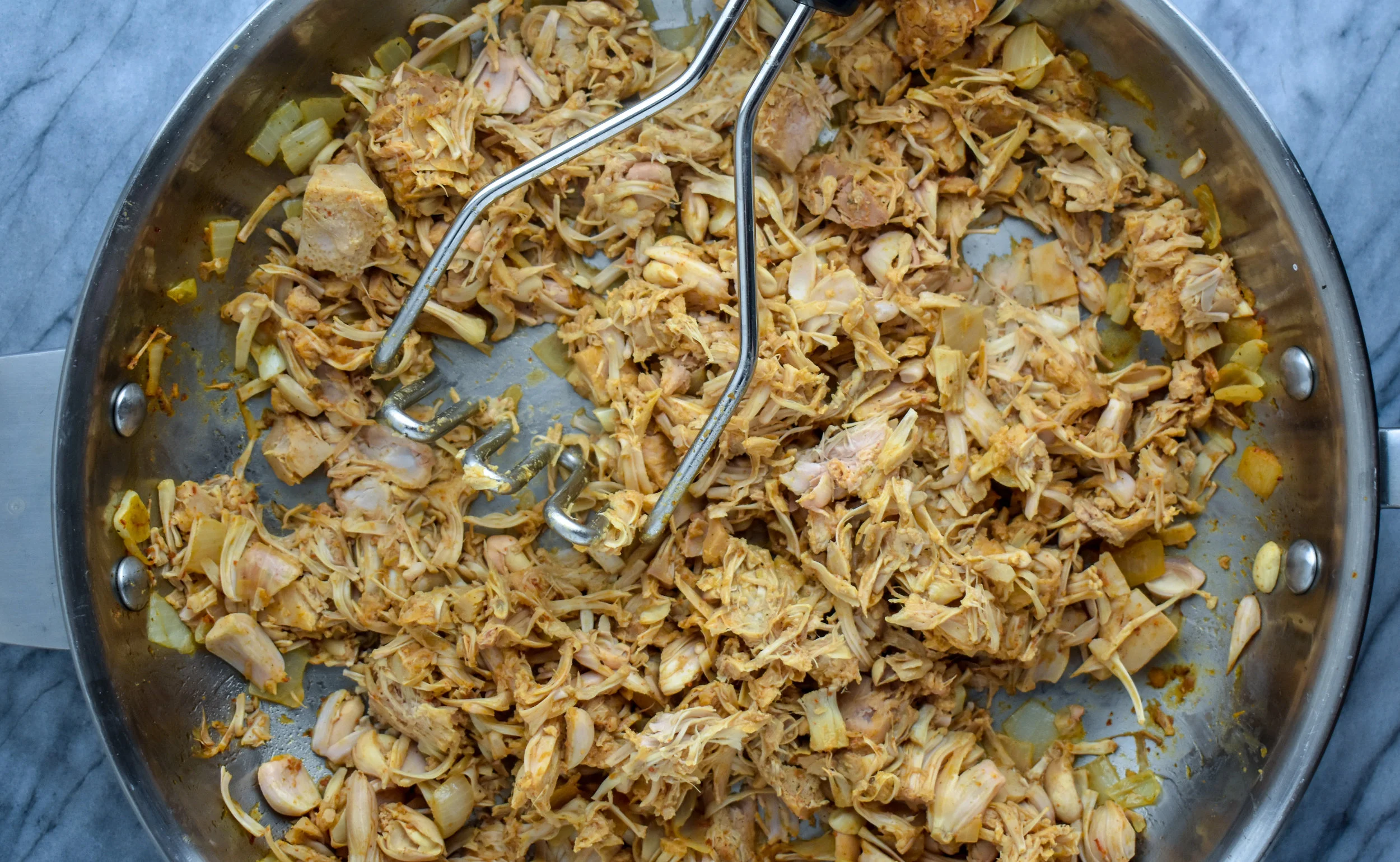 2. Next, using a potato smasher, large spoon or fork, or other instrument, begin to smash the jackfruit and it will form a shredded style.
