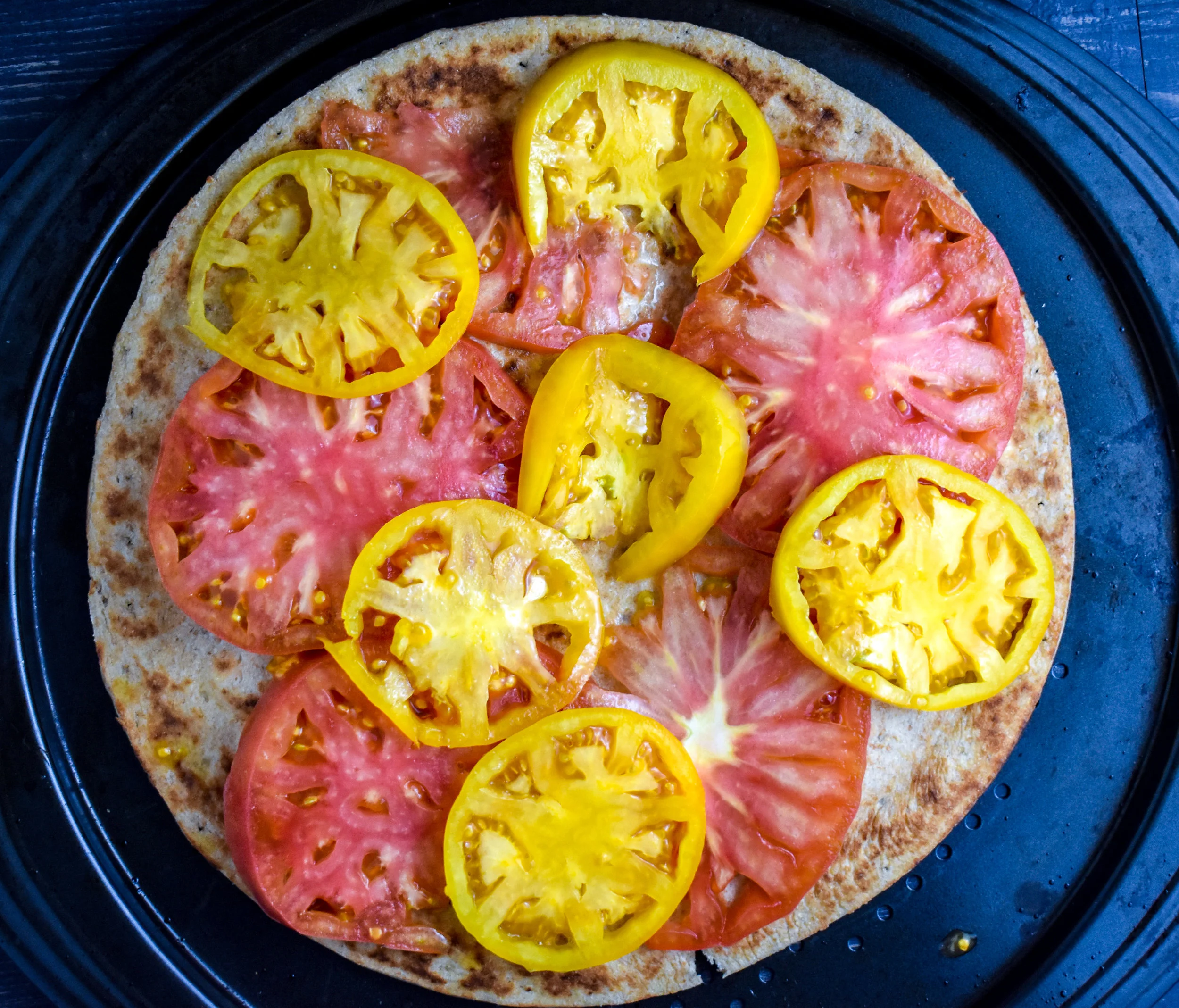 3. While the jackfruit cooks, add heirloom tomato slices to crust. Make sure to deseed (remove the seeds and juicy parts). If you don't it will make the pizza soggy.
