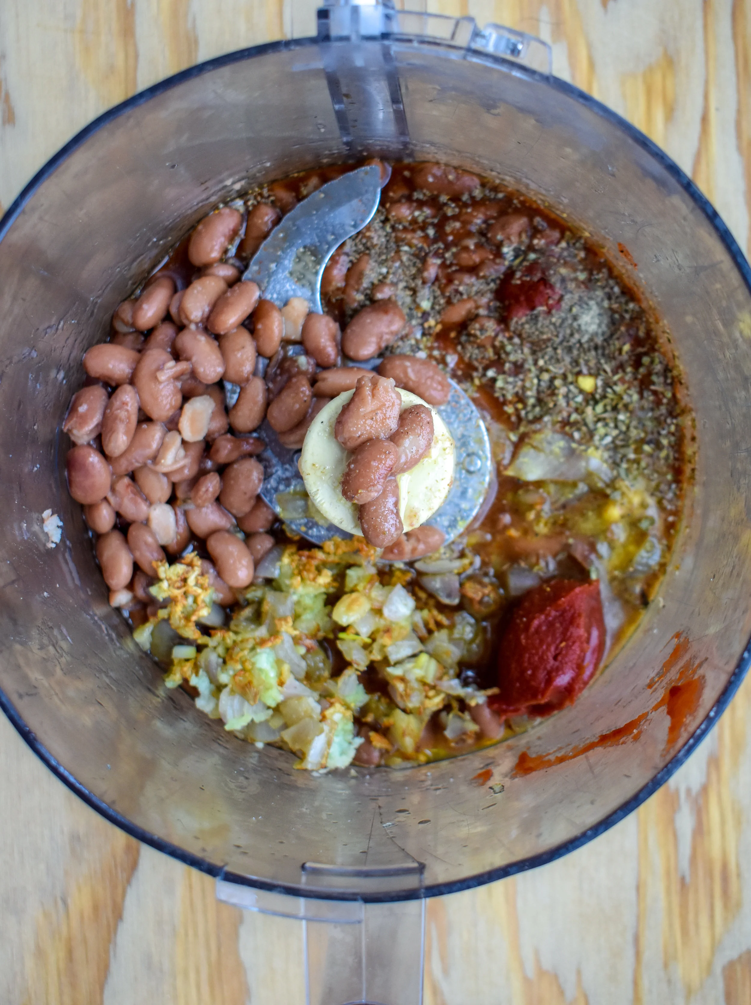 2. Add cooked onions, garlic, pinto beans, water, aminos, tomato paste, and spices to a food processor or high-speed blender. Blend until liquid - about 10-15 seconds.