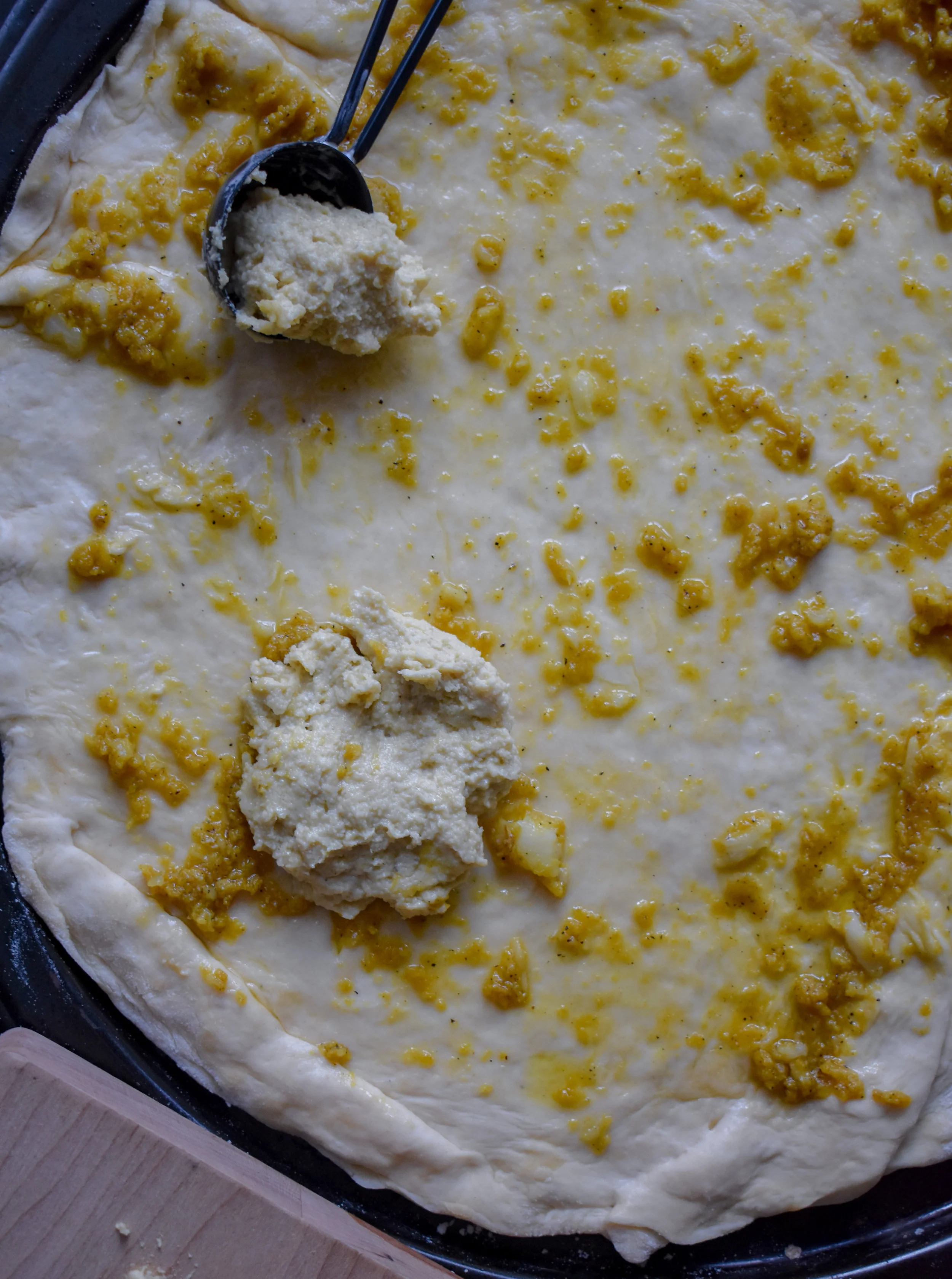 8. After rolling out the dough, spread on the truffle garlic oil. Next, using a tablespoon scoop out large chunks of the mozzarella cheese and place onto the dough. Use a finger or the back of the tablespoon to gently flatten the cheese down so it creates little mozzarella cheese chunks. Continue this all over the pizza. I usually use about 3/4 of the cheese and leave open spots for other toppings.
