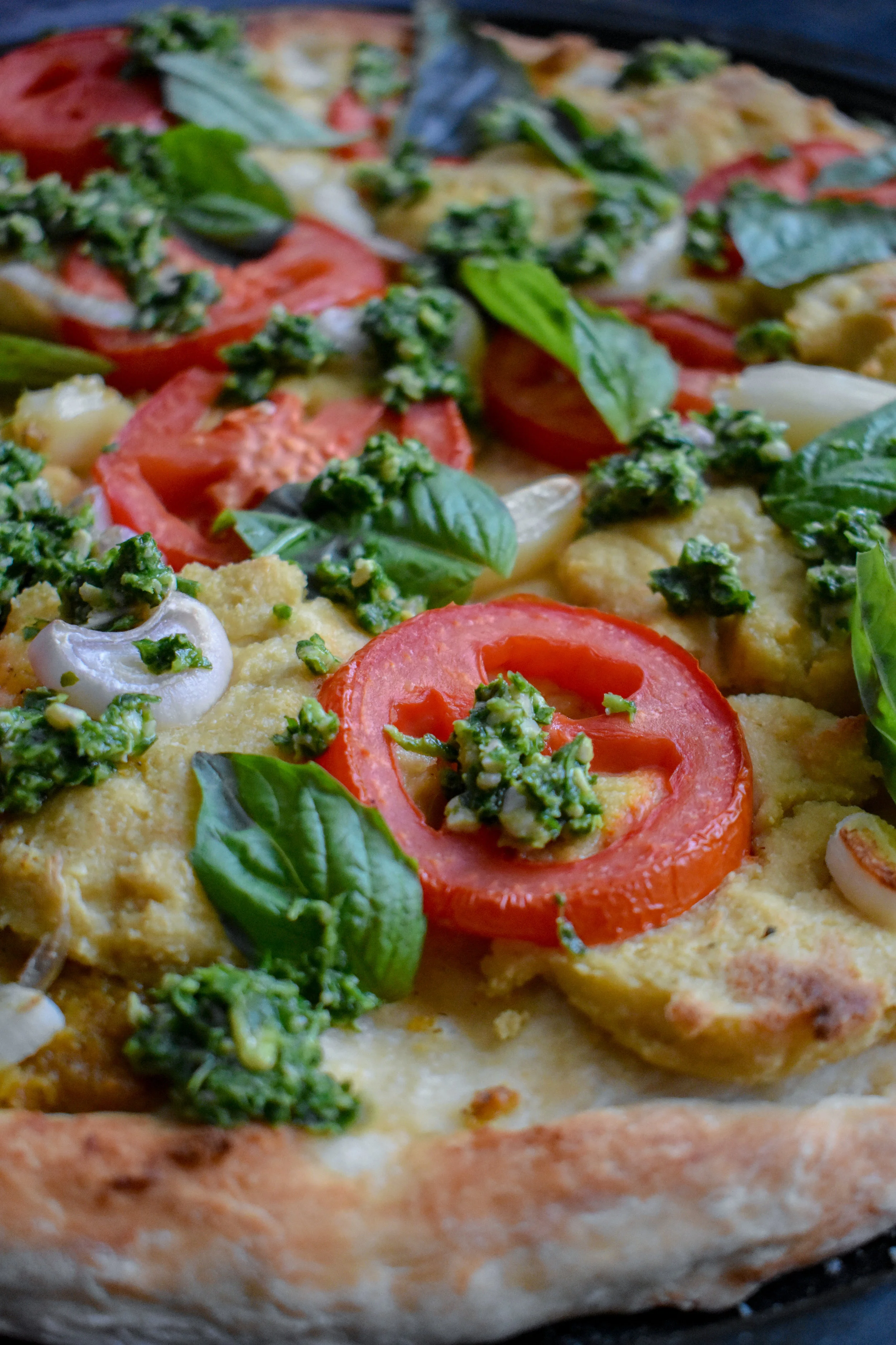 9. To finish, top with sliced roma tomatoes, the rest of the garlic, shallot strips, and pop into the oven at 475F for 10-12 minutes. I broil the pizza at 525 for a last 2 minutes. Once out, top with fresh basil immediately (the heat will cook it slightly) and when ready to serve sprinkle on some pesto. Enjoy!