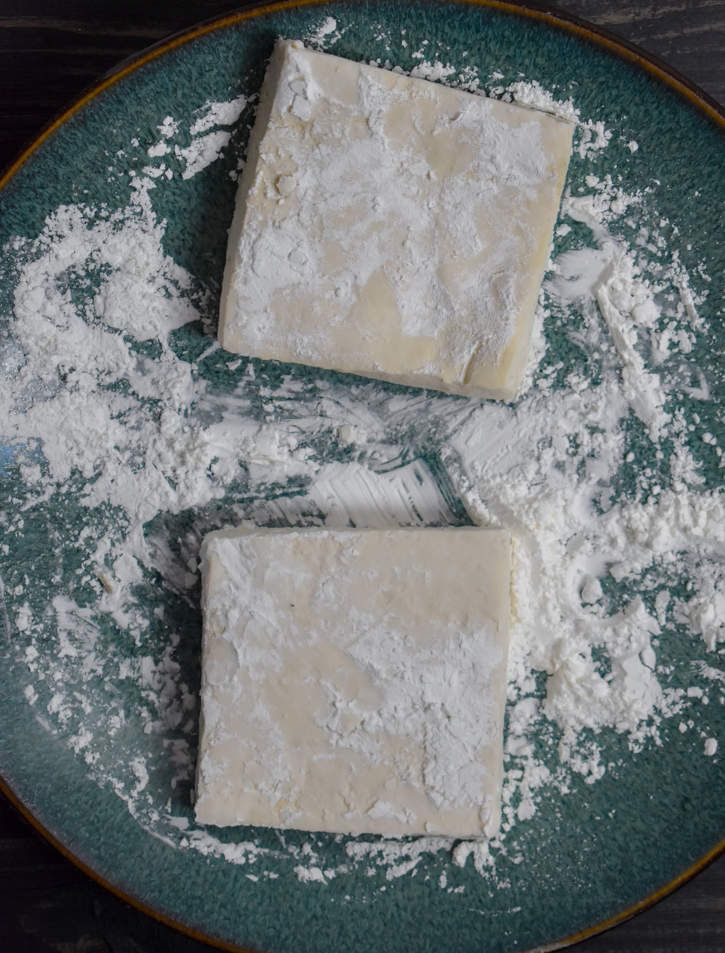 4. Next, slice the last 1/5 of the tofu block off to create a square shape. Then flip on the width side and slice in half so you have two equal squares. Mix the tofu with cornstarch to create a coating on the tofu.