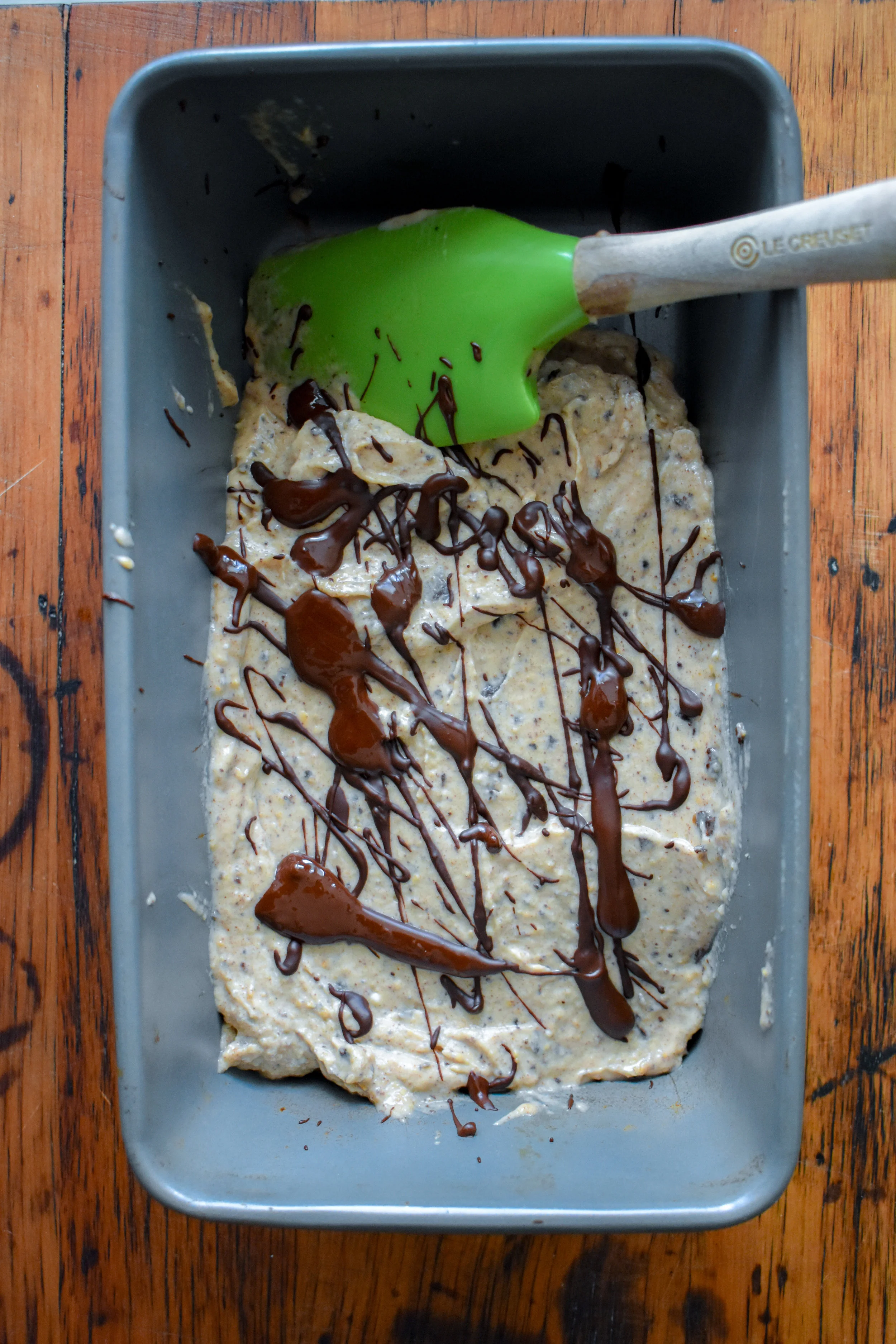 3. If you haven’t yet, melt your dark chocolate. I just throw mine in the microwave for 50-60 seconds and mix it. You can also melt it over a small pot of boiling water in a heat-resistant bowl. Once done, transfer the ice cream to a parchment-lined bread pan or rimmed pie pan. The parchment helps it not stick to the sides. Then, drizzle the melted chocolate over the top with a spoon or fork.