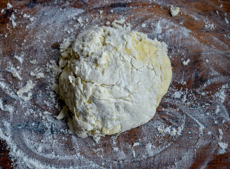 5. Form the biscuit mixture into a ball and place on a flour lined surface. Flip the mixture 2-3 times on the surface and let it rest for a few minutes .
