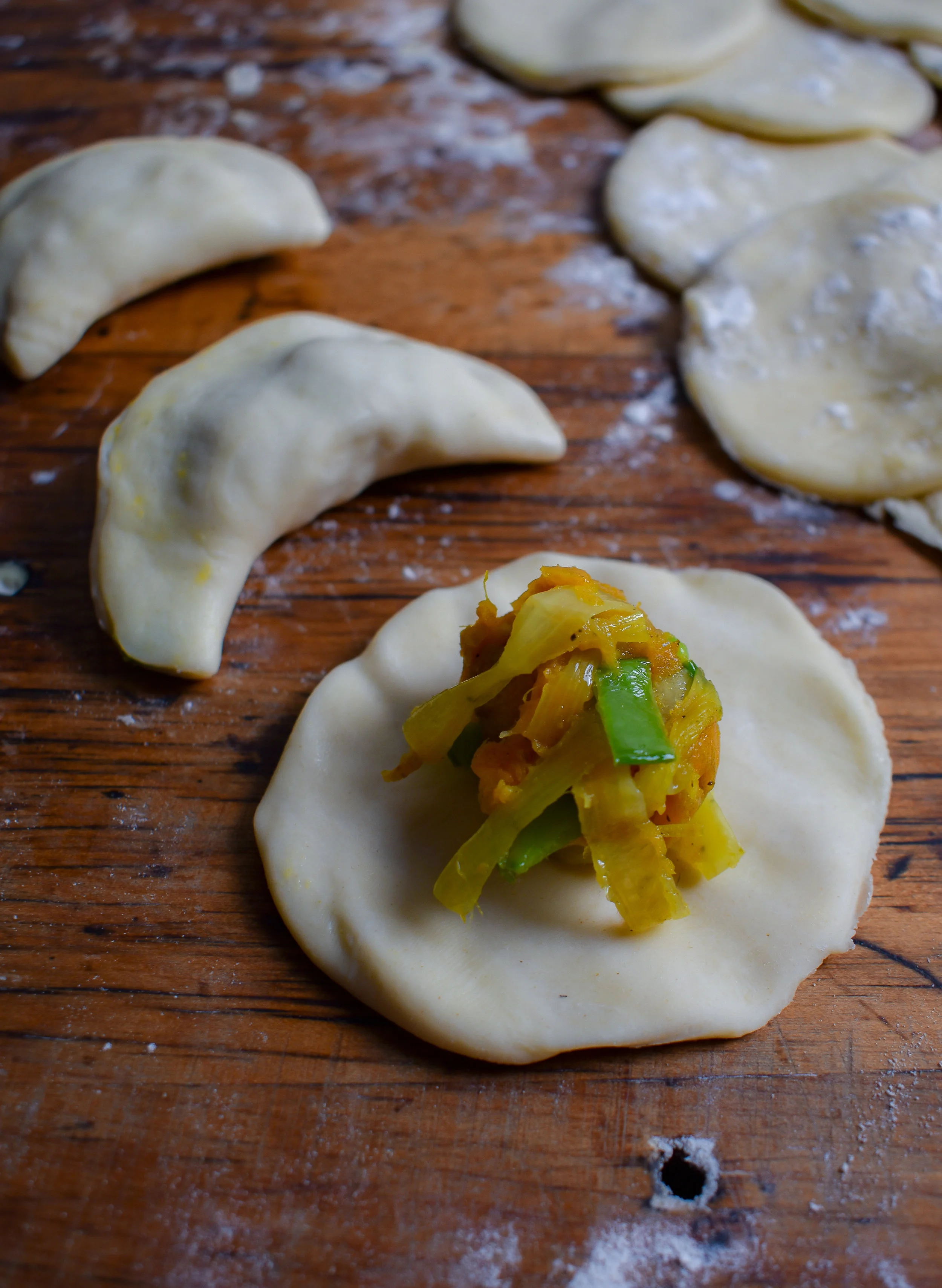 9. To form the pierogis, mix the leeks + potato mixture. Then using a table spoon, scoop out a small amount of the mixture and place it on the pierogi dough. To form press the mixture down with your thumb and fold one side over to the other. Pinch the edges. Then use a touch of water on the fingers to run over the pinched edge.
