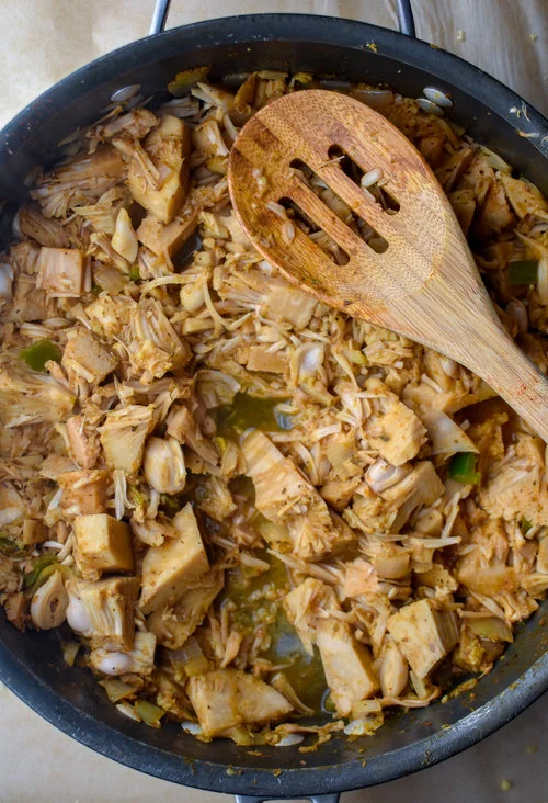 2. Next, add in the broth + orange juice + lime juice, turn your heat to low once it starts to simmer, cover and cook for 20-25 minutes. You want to cook it until the jackfruit is really soft and starts to break down, but you want it to have some firmness left so that its not soggy. Use the back of a wooden spoon or potato masher to break it down. Set aside.
