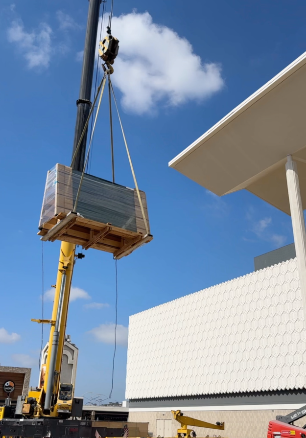 A crane lifts an a-frame shaped crate carring glass panels