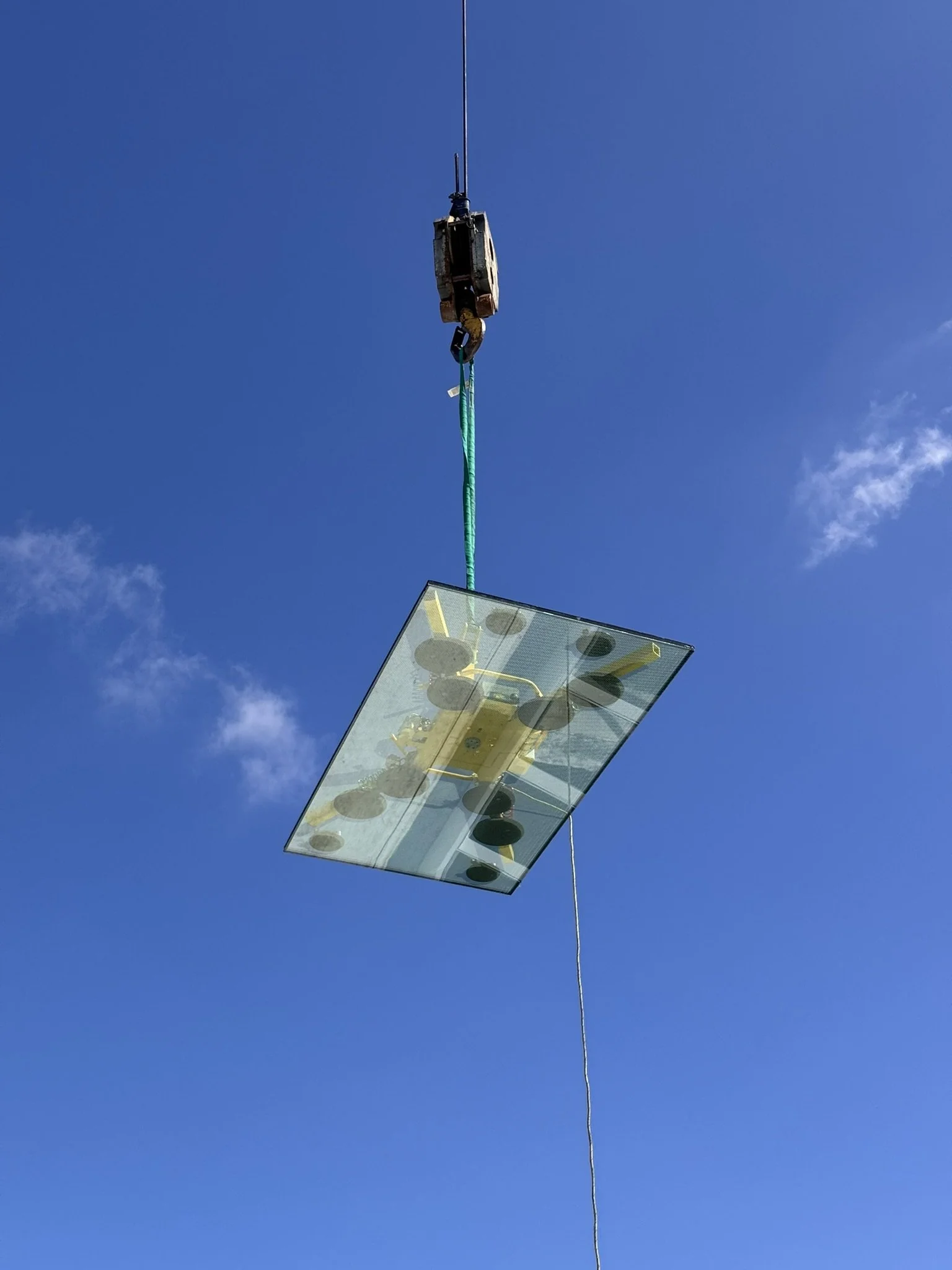 A solar panel array suspended in the air by a crane or hoist against a blue sky.