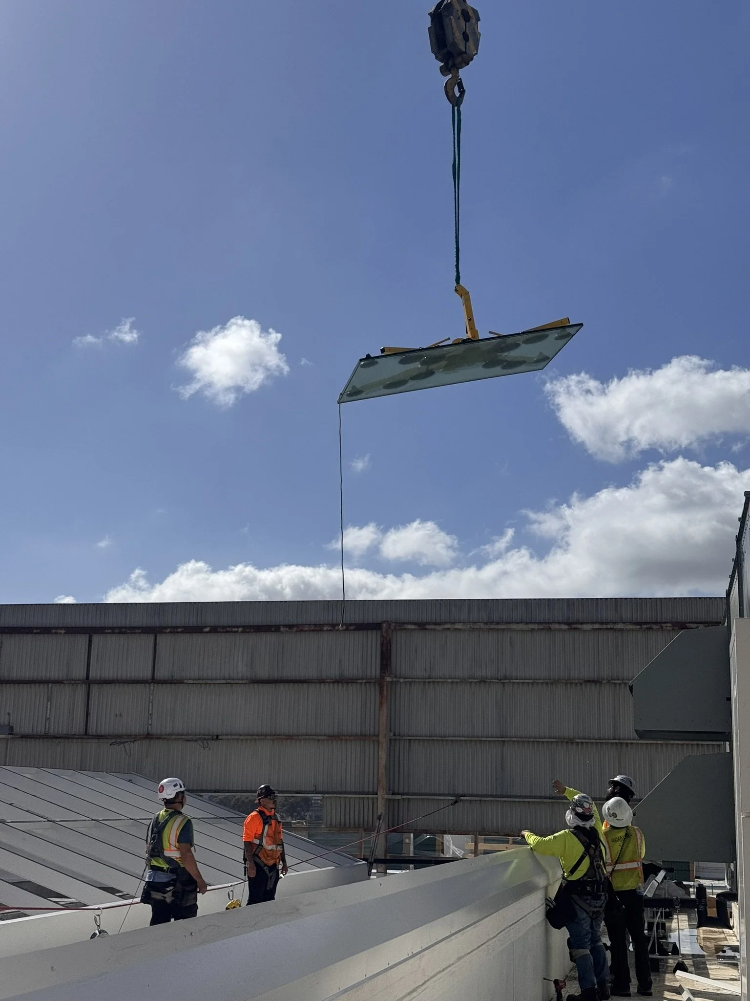 Inter-sky crew reaching for a glass panel suspended by a crane, about to place it into the skylight.