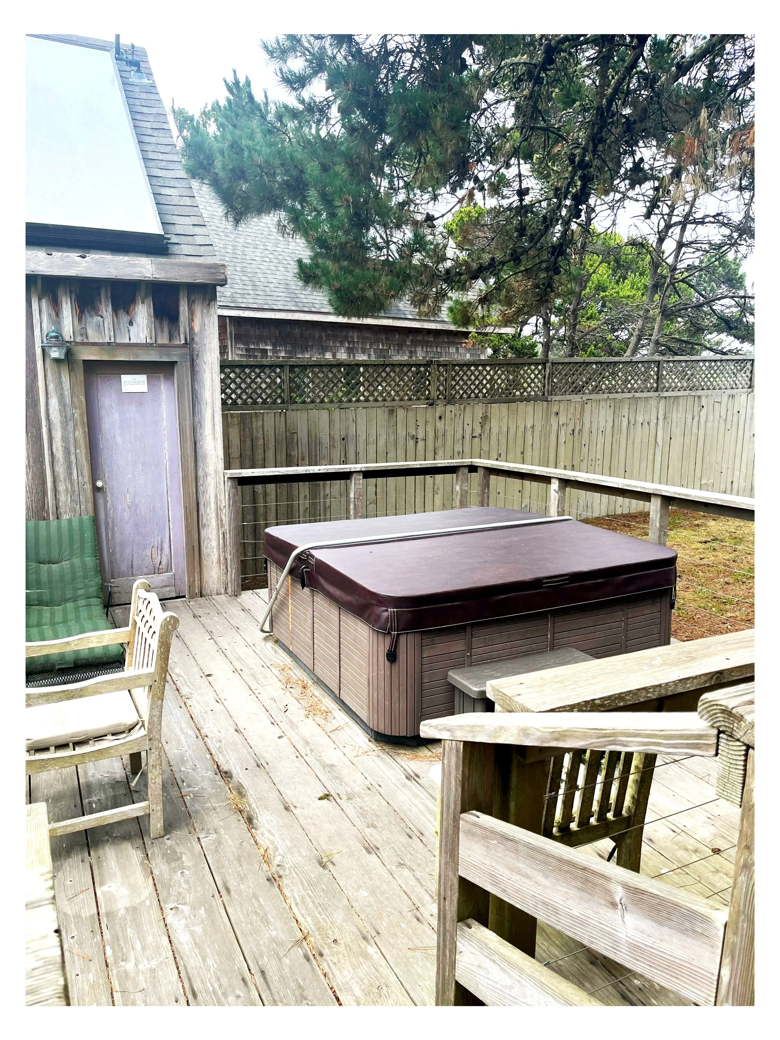 A backyard wooden deck with outdoor furniture, including a hot tub, surrounded by a wooden fence and trees at B. Bryan Preserve in Point Arena, California at one of the cottages.
