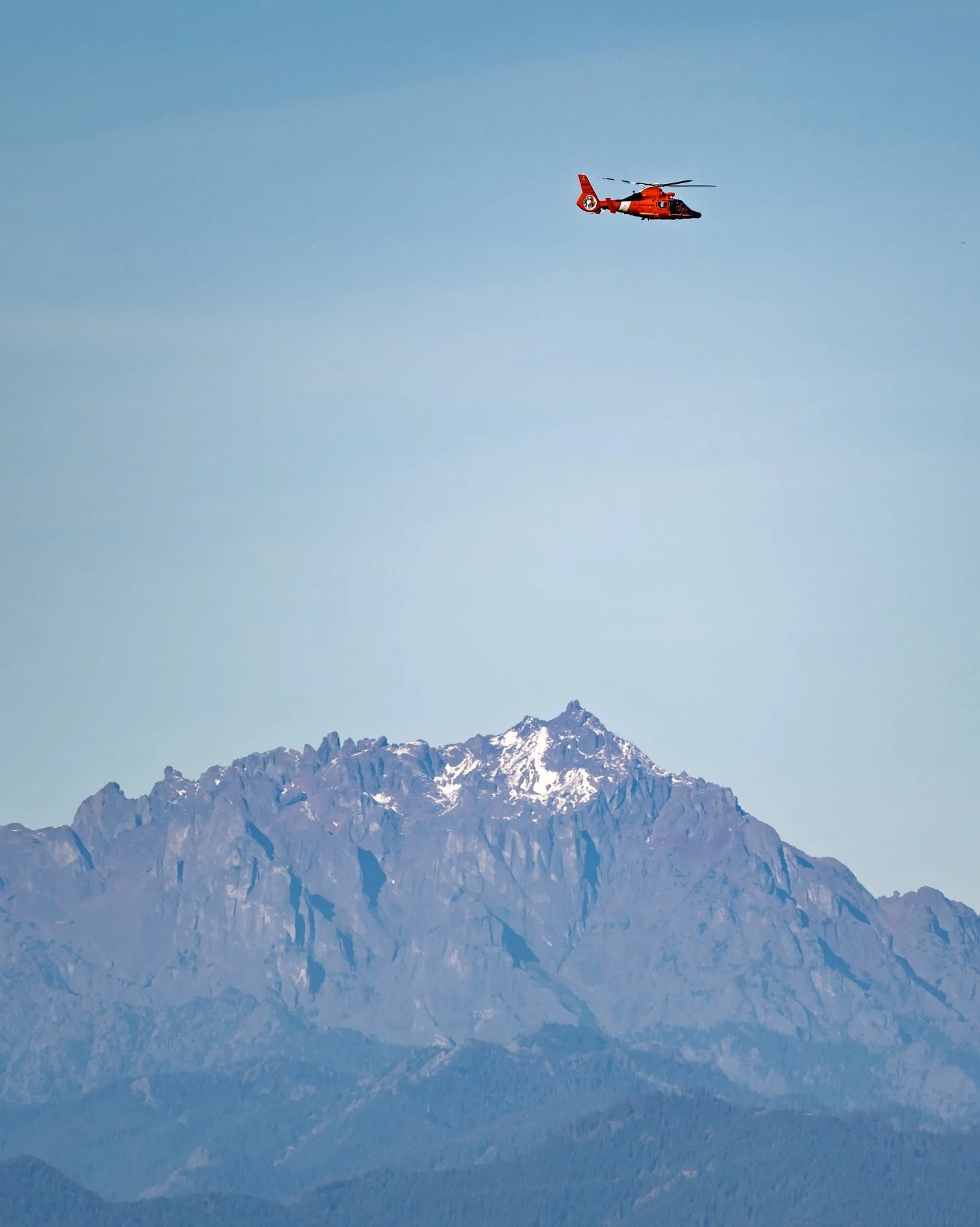 A @uscgpacificnw helicopter passing by the mountains