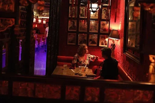 A couple dining inside an intimate red alcove booth framed by carved wood at The Formosa Cafe.