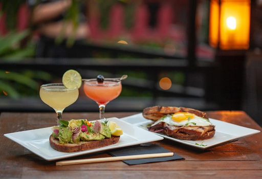 Two handcrafted cocktails served with avocado toast and a fried egg sandwich on the outdoor patio at The Formosa Cafe.