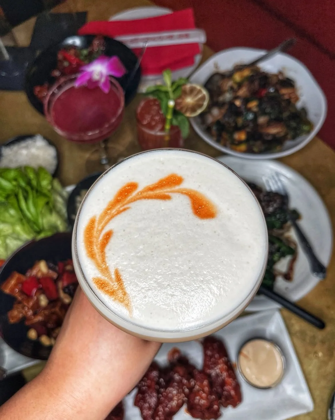 A foamy cocktail held above a table filled with small plates and other cocktails at The Formosa Cafe.