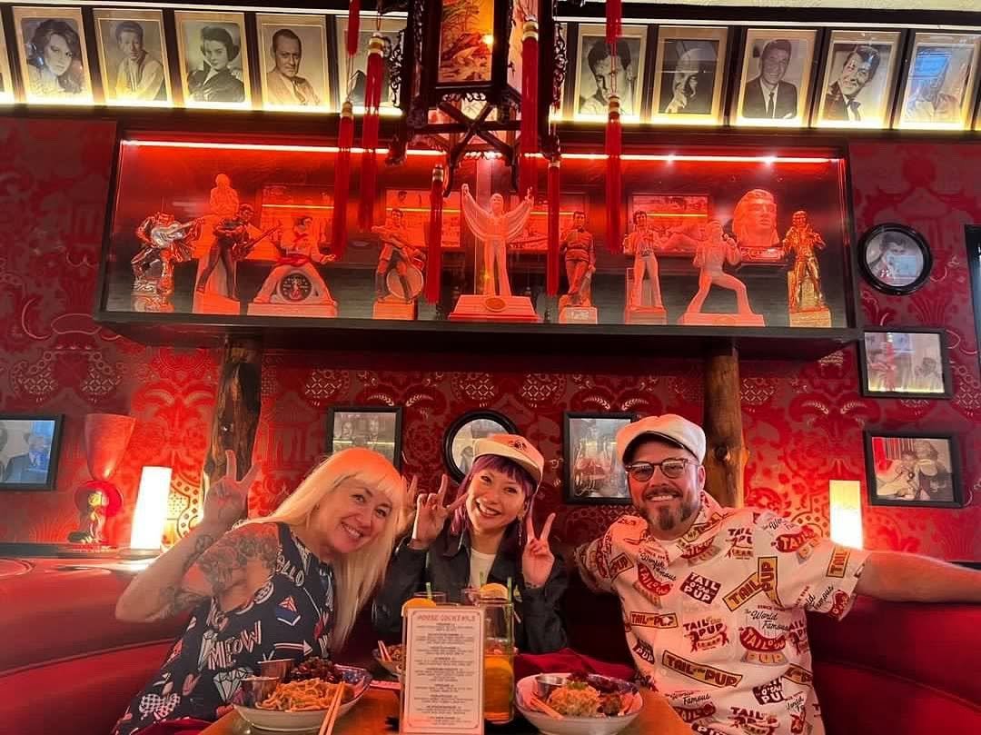 Three guests smiling inside a historic red booth at The Formosa Cafe surrounded by vintage Hollywood memorabilia.