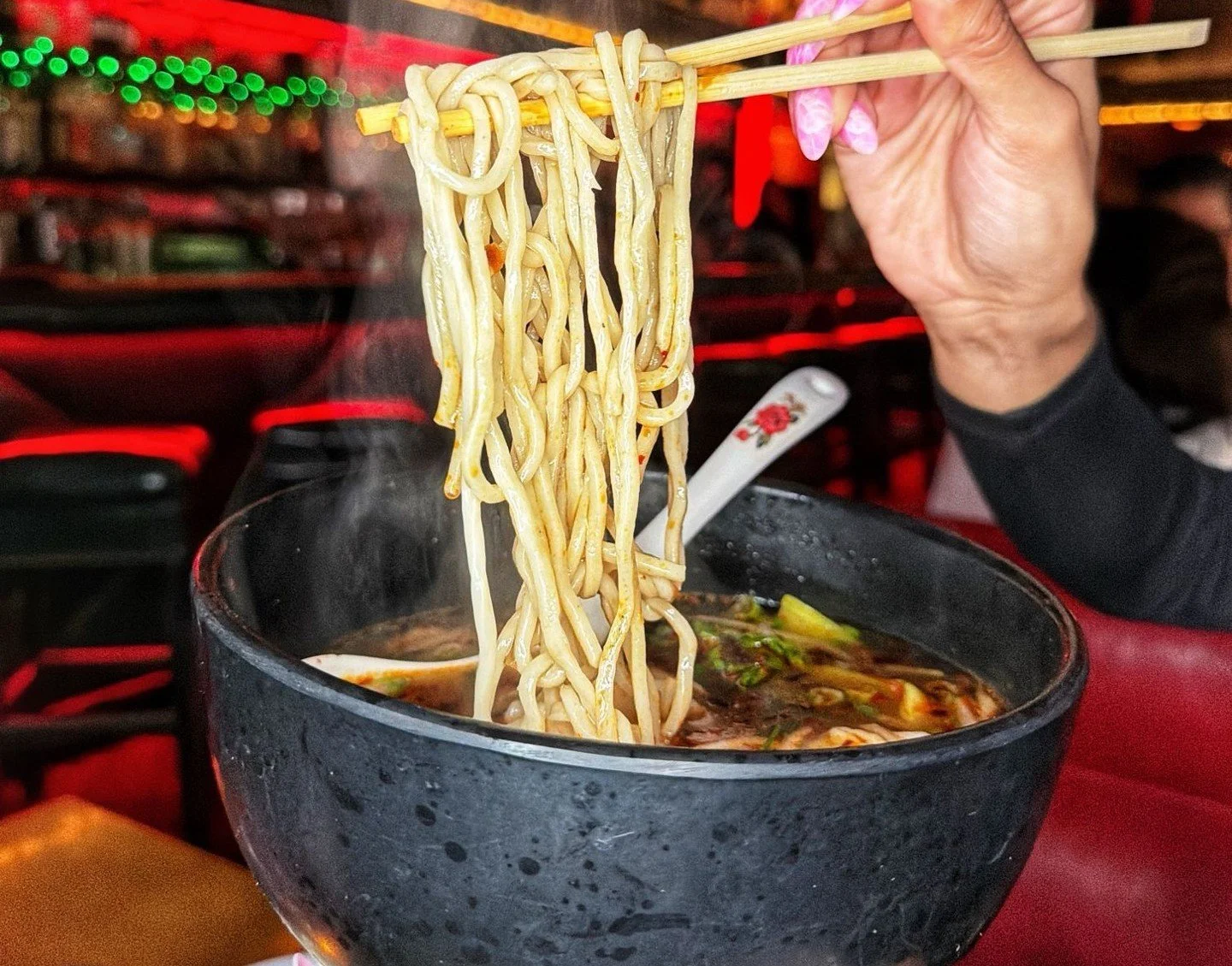 A hand holds a bowl of soupy noodles, picking them up with a pair of chopsticks at The Formosa Cafe.