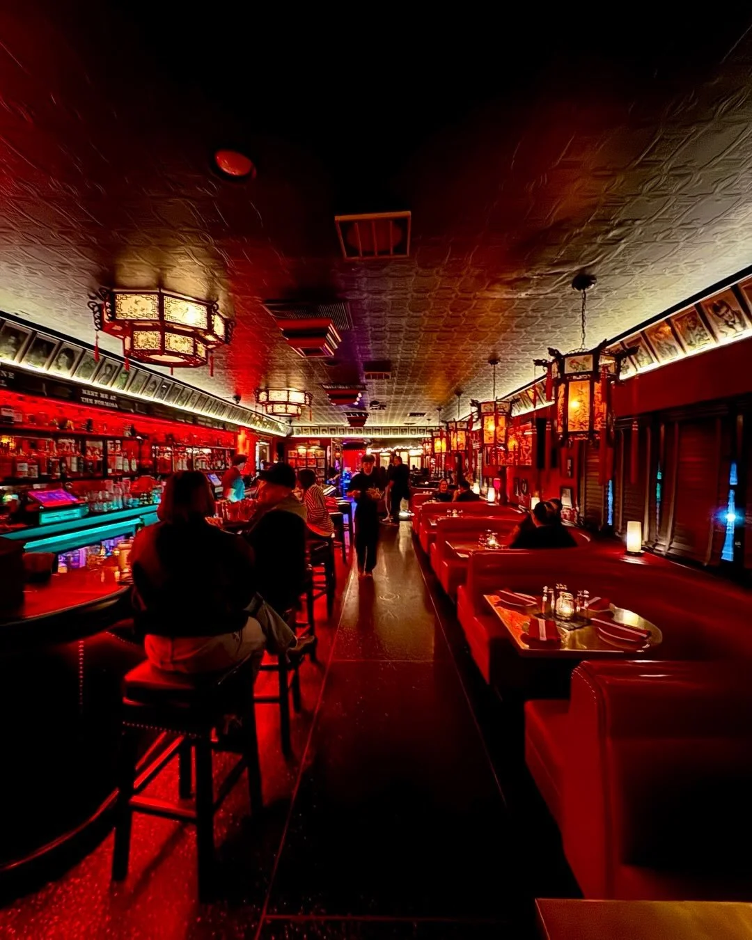 The Formosa Cafe's warmly lit interior features red booths, a bustling bar, and traditional Chinese lanterns suspended from the ceiling.