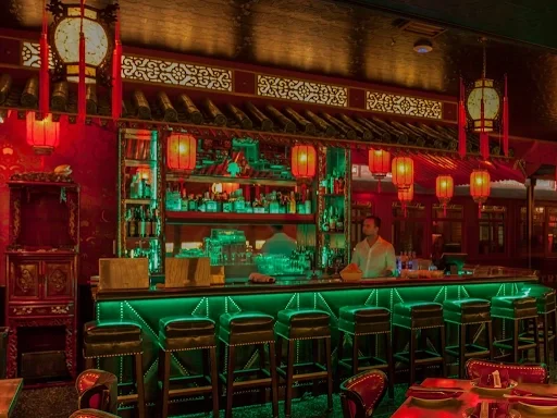 A dimly lit Formosa Cafe restaurant bar featuring glowing green lighting, red lanterns, and leather barstools.