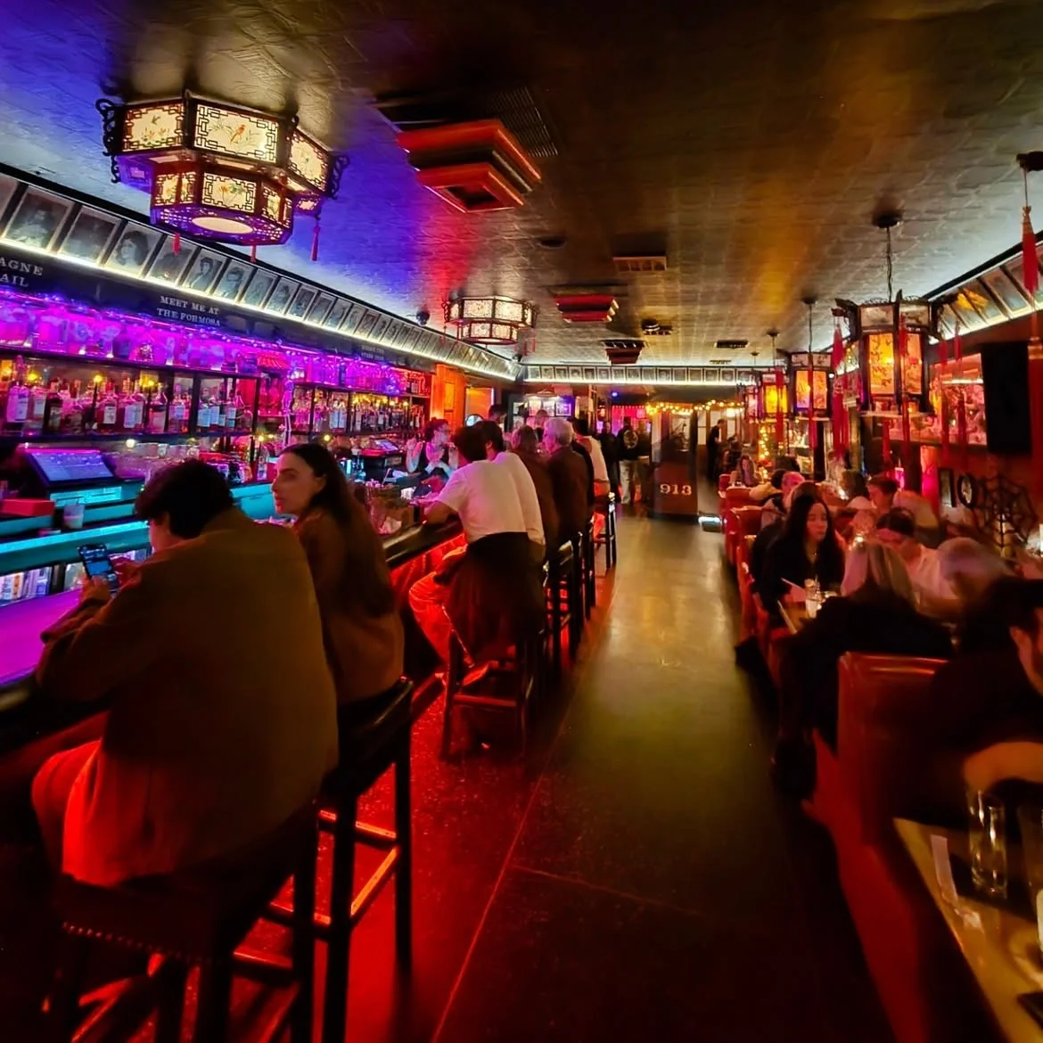 Bustling neon-lit bar scene inside the iconic Formosa Cafe with patrons enjoying the atmosphere.