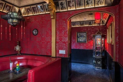 Red leather booth with cocktails in a room with ornate red wallpaper and framed celebrity portraits at The Formosa Cafe.