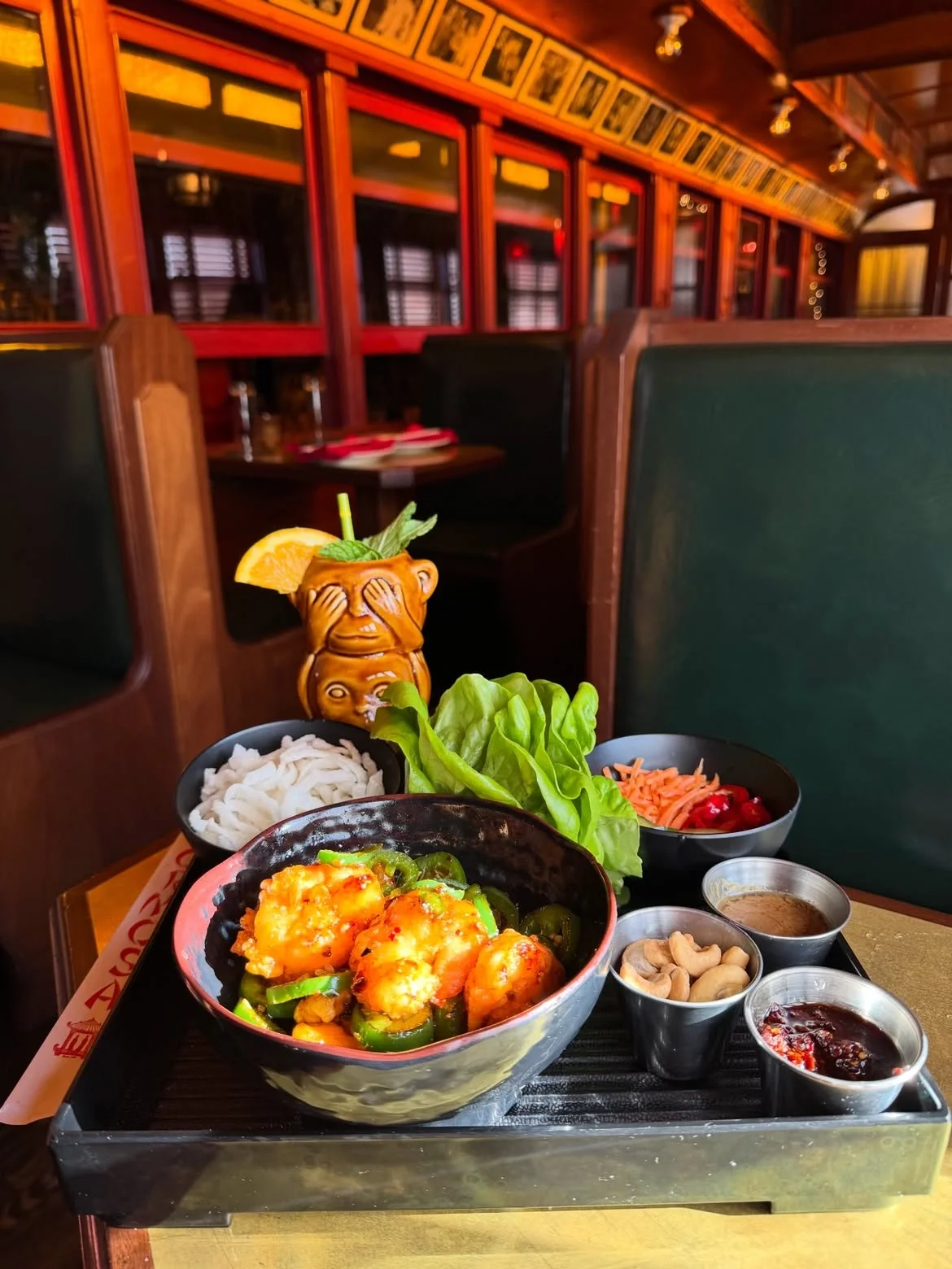 A spread of Asian dishes and a monkey tiki mug inside a vintage train booth at The Formosa Cafe.