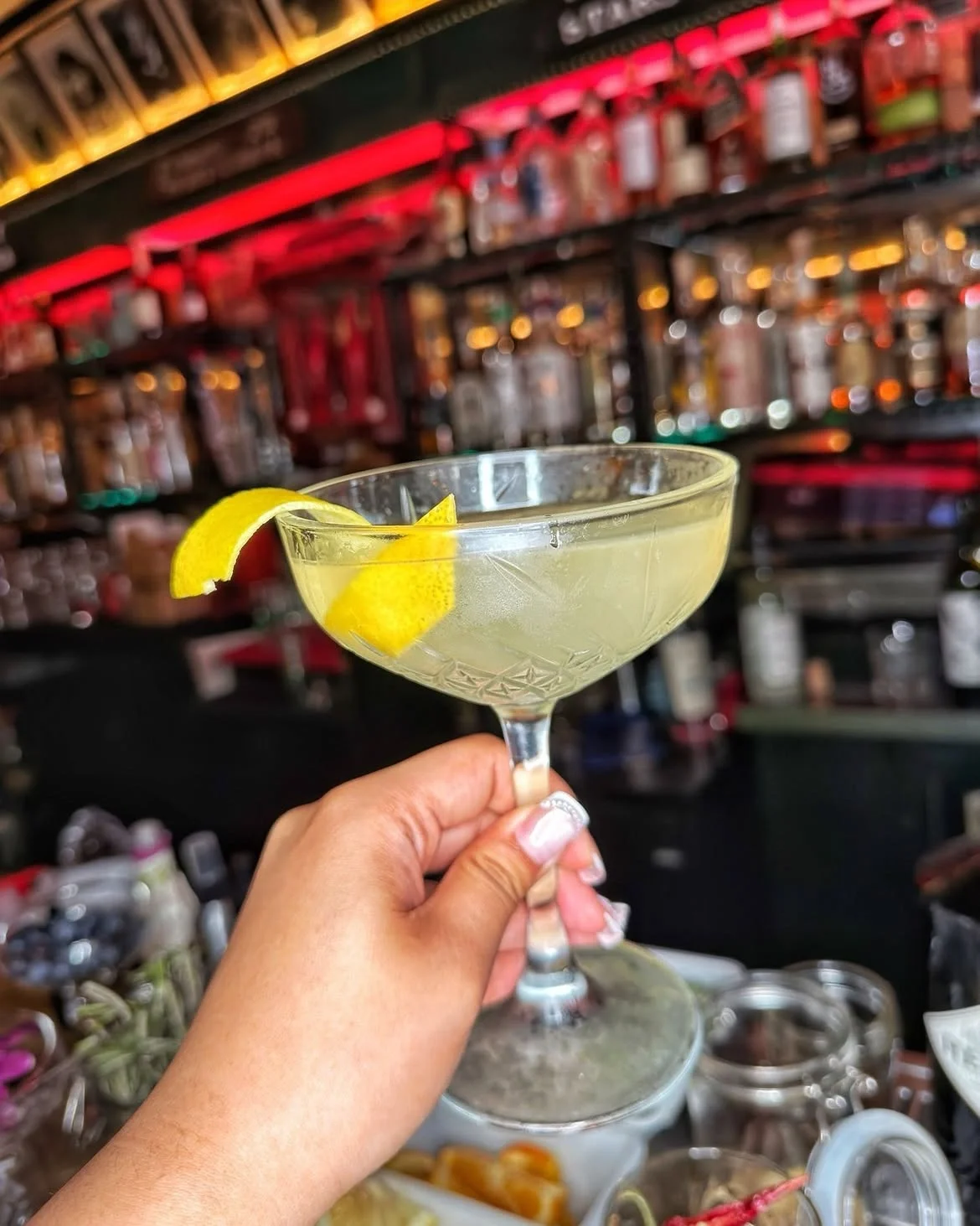Hand holding a clear cocktail with a lemon peel garnish at the Formosa Cafe bar.