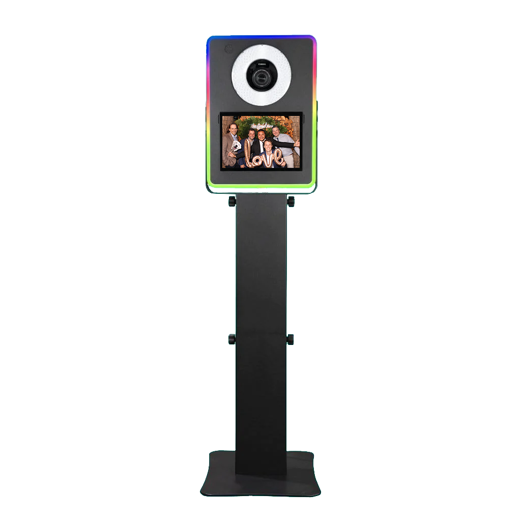 A photo booth with a camera on top and a touchscreen display showing a group of people holding signs and decorations with the word "love".