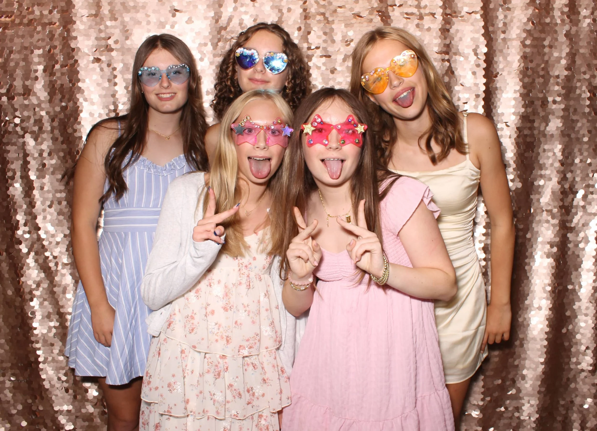 Five teenagers wearing colorful star and heart-shaped sunglasses posing at a Fancy Booth luxury photo booth in Seattle with a rose gold sequin backdrop.
