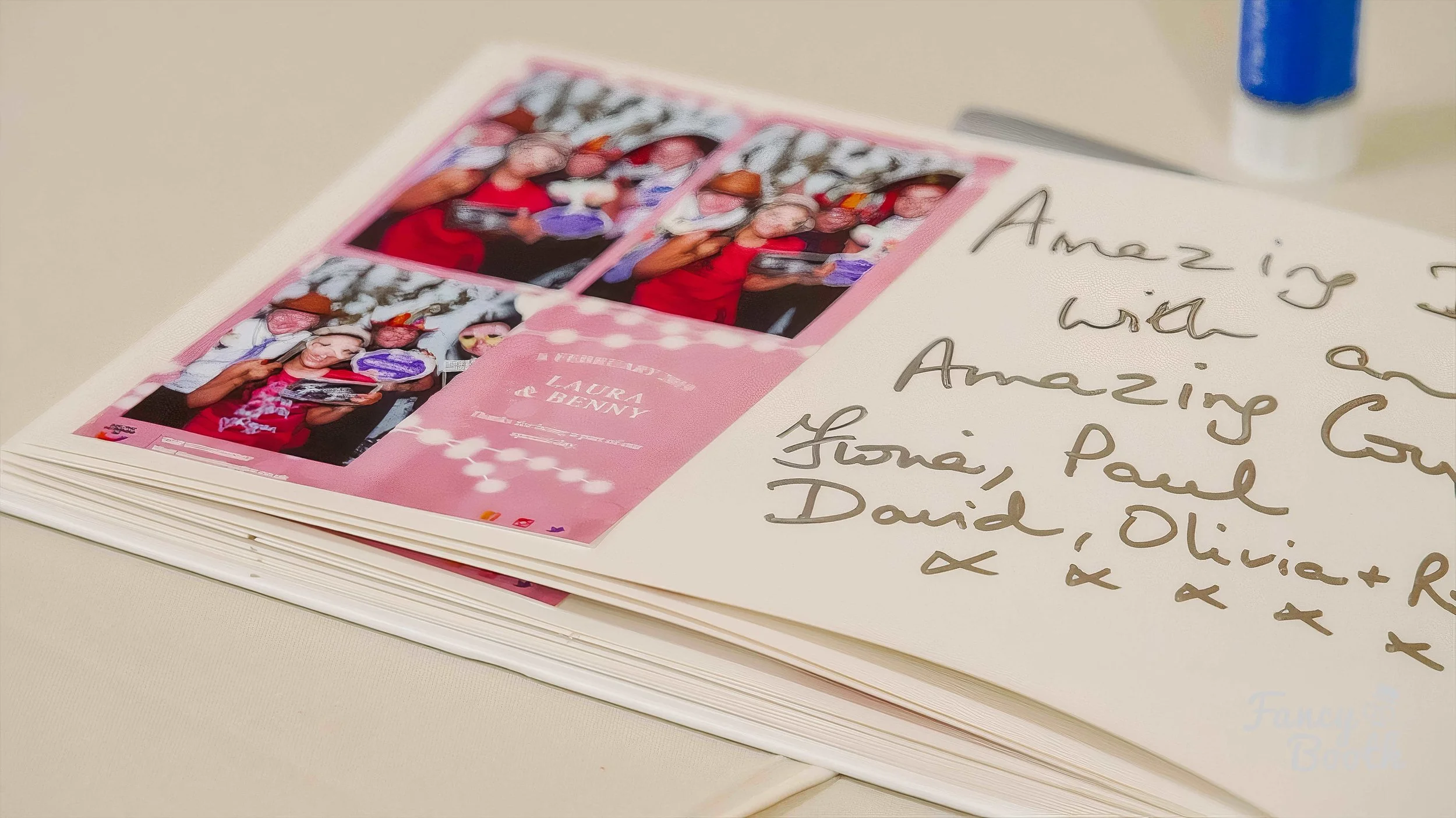 Open guest book with handwritten messages and printed photos on a white page, with a blue marker in the background.