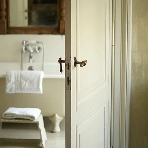 The simplicity of a neutral color palette allows one to appreciate the little things: Vintage hardware, texture of fabrics, and objects such as a rustic, antique mirror just beyond the doorway.