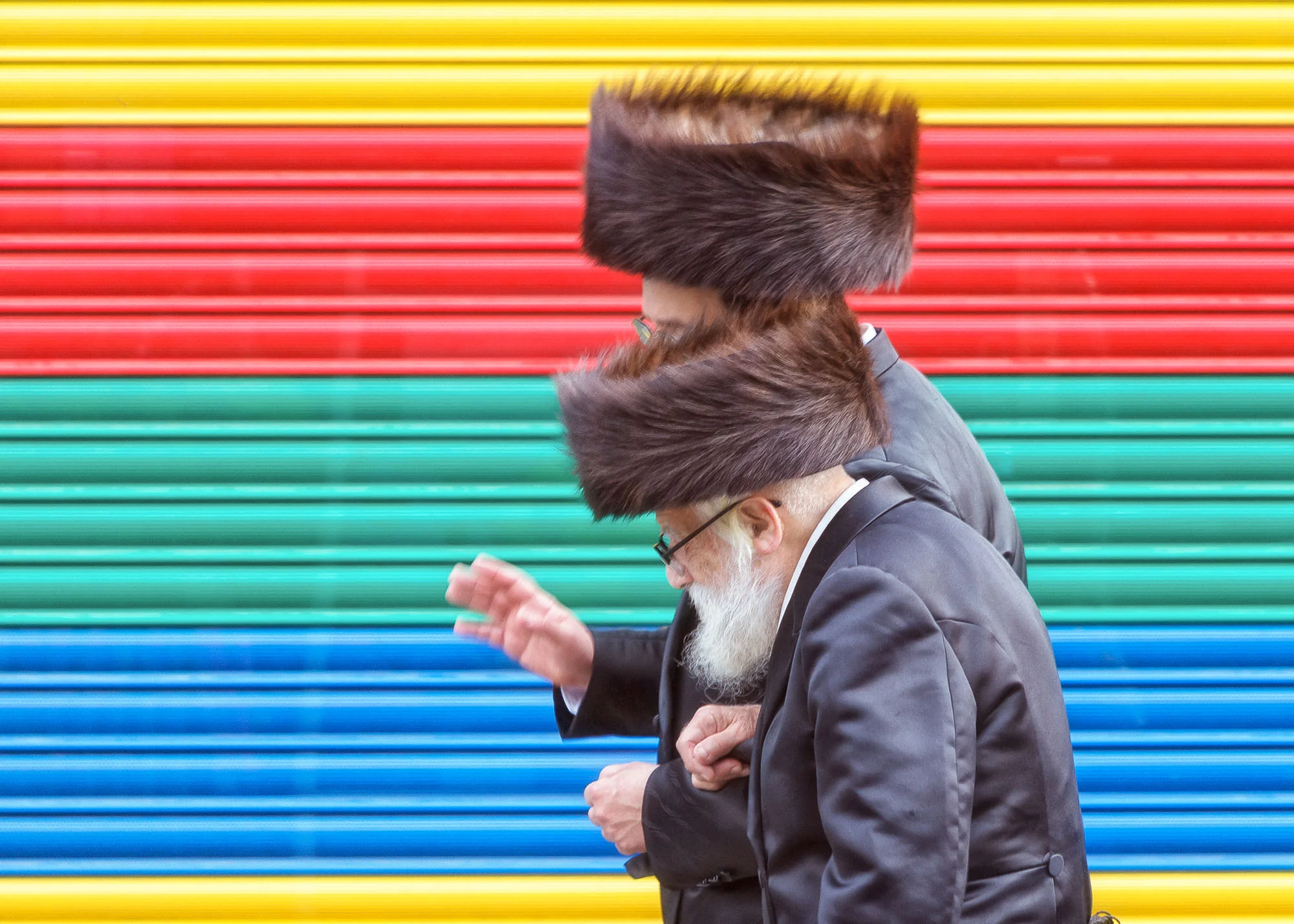 Stamford Hill. Ultra-Orthodox Jews on the streets with a rainbow garage as background