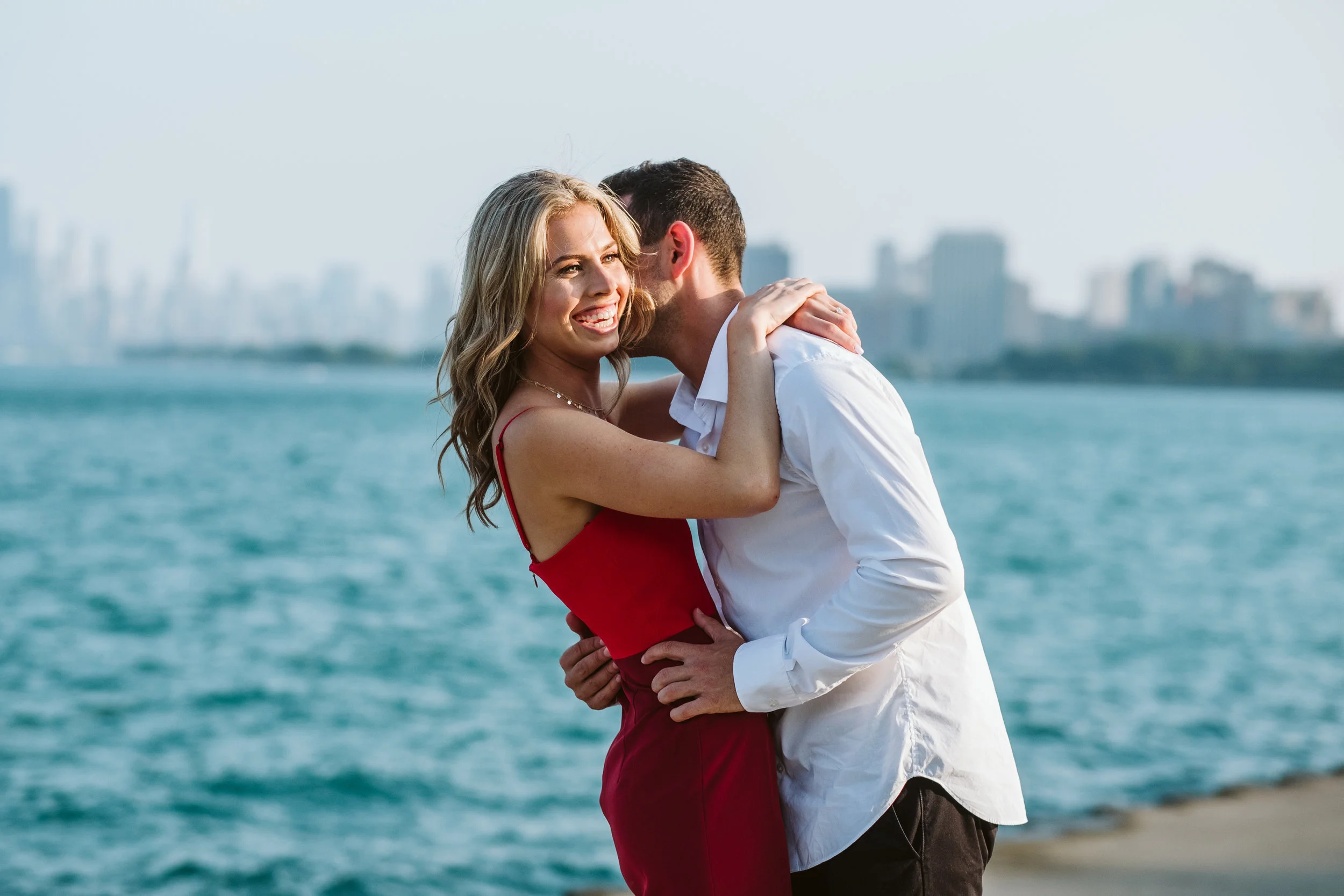 Couple doing Lake Michigan engagement photos while giggling in front of the Chicago skyline. By Michael & Kristin Chicago Photographer and Videographer 