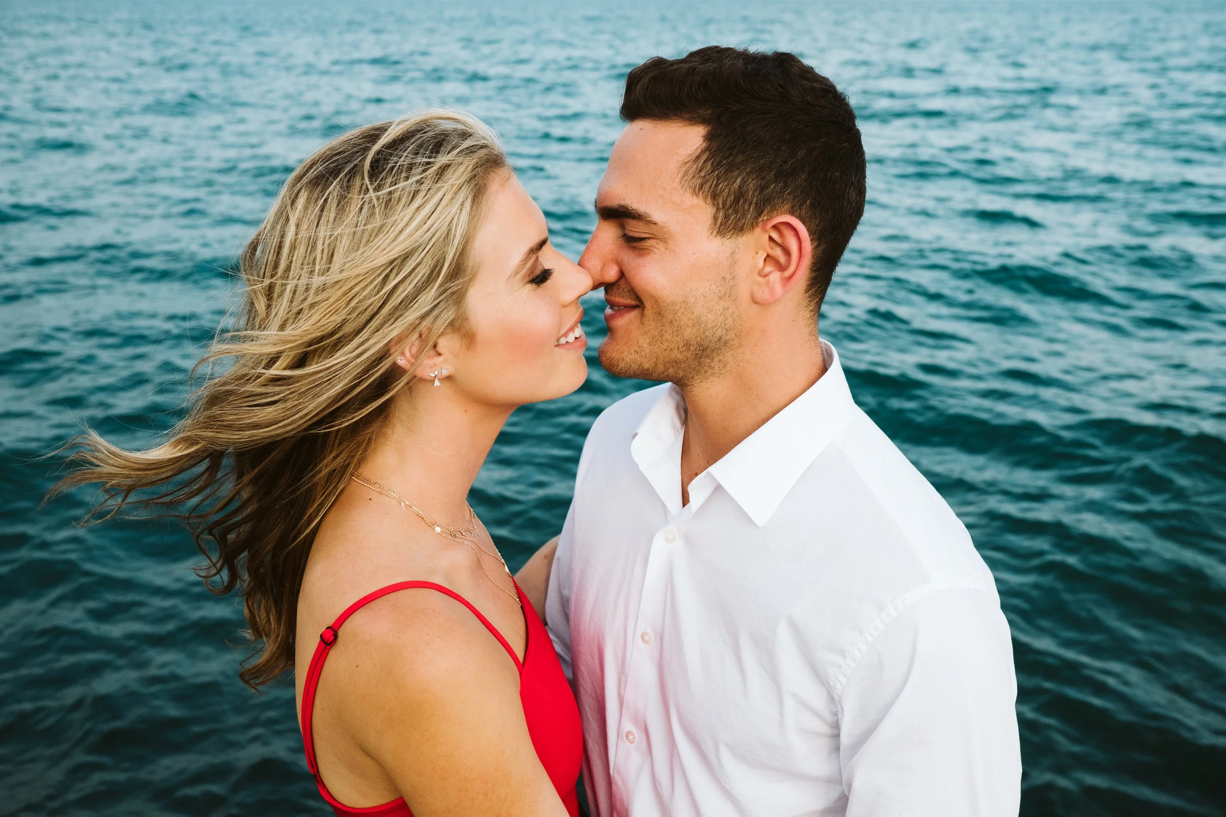 Engagement photo of a couple almost kissing in front of the deep blue waters of Lake Michigan. By Michael & Kristin Chicago Photographer and Videographer 