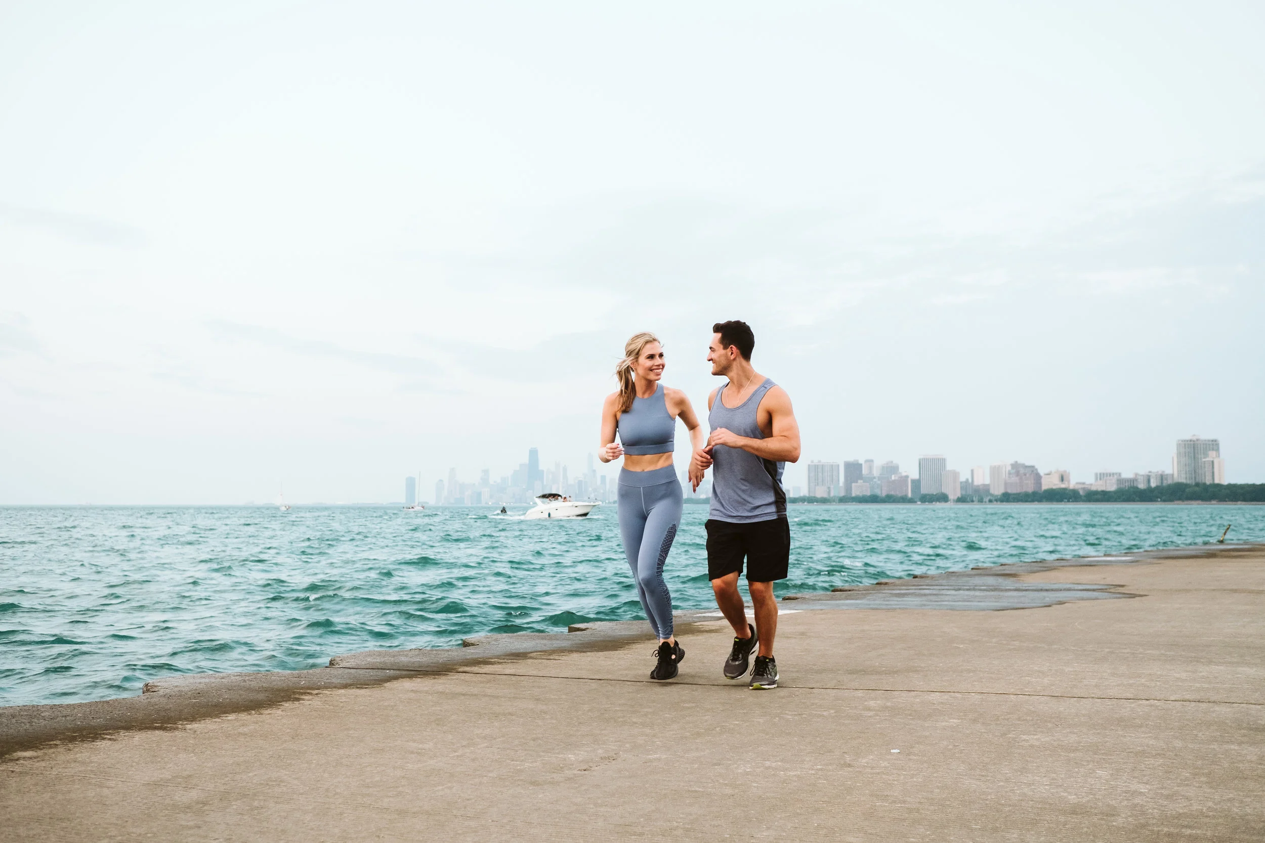 Lake Michigan engagement photos featuring a couple running along Lakeshore Drive with the Chicago city skyline in the background. By Michael & Kristin Chicago Photographer and Videographer 