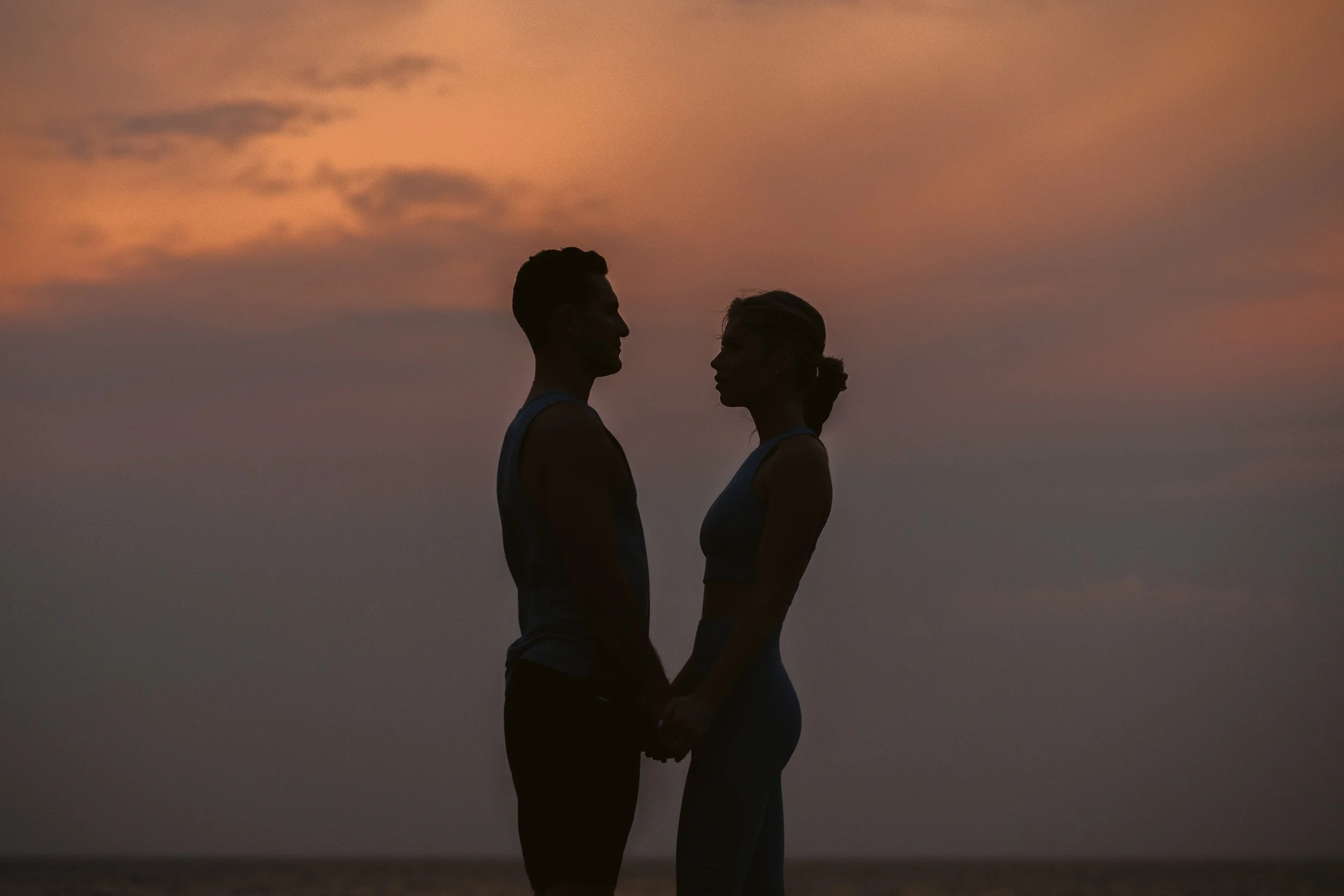 Sunset during Lake Michigan engagement photos session featuring silhouettes of the couple look towards each other against the backdrop of the sky. By Michael & Kristin Chicago Photographer and Videographer 