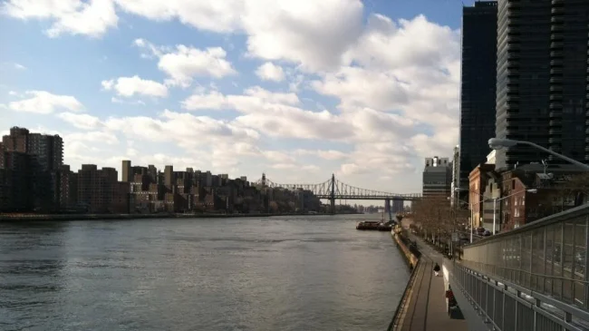 Looking south along the East River, below a blue sky with fluffy white clouds.