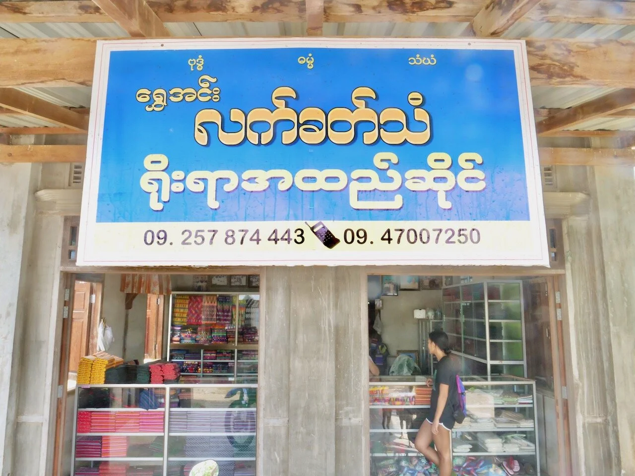 The storefront is facing the main road in Mainaung Village, and it has all the colorful fabrics on display.