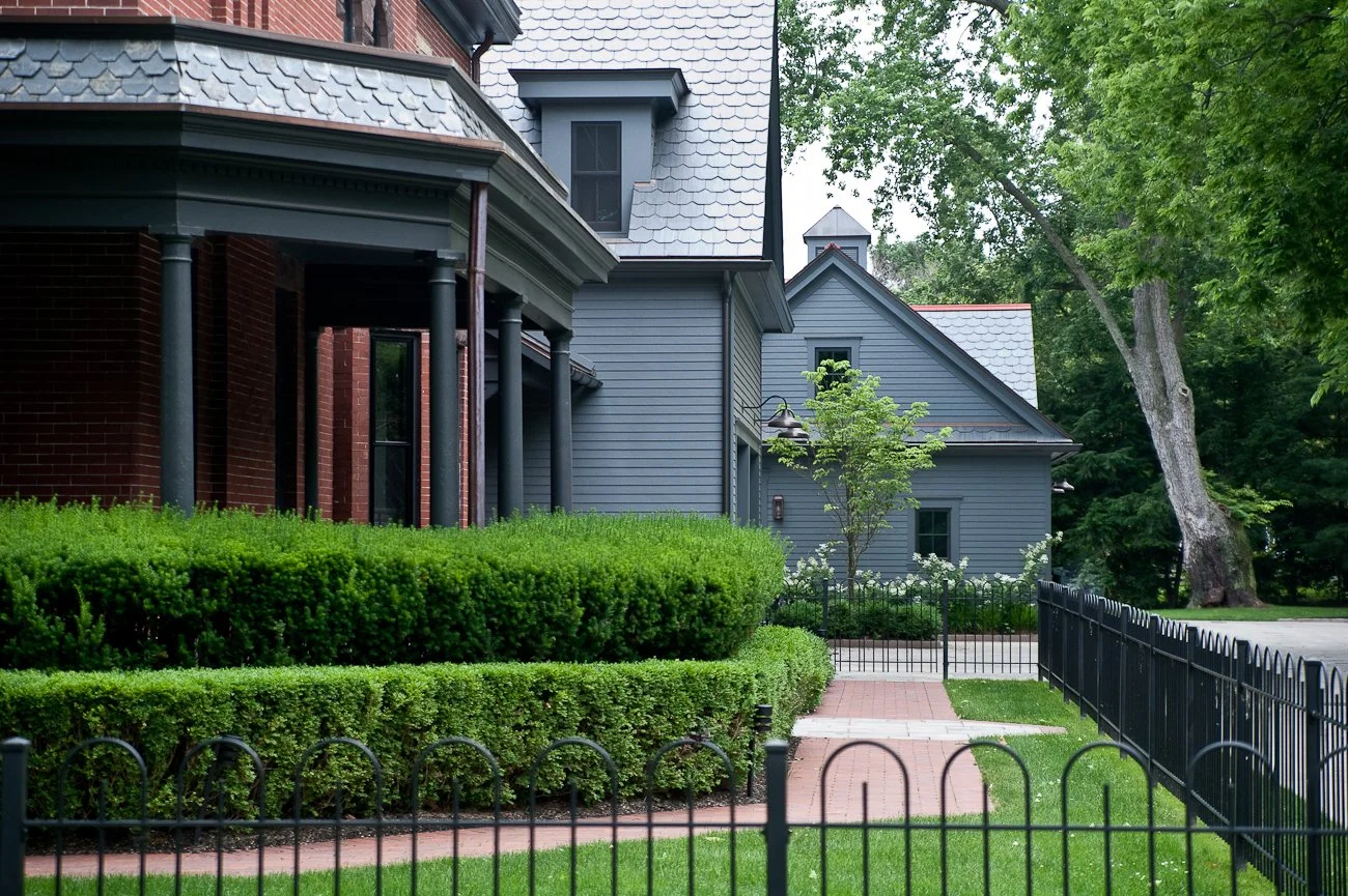 A large estate entryway with hedge bushes and wrought iron fence.