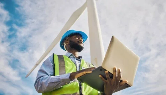 Man looking at a laptop with a wind turbine in the background