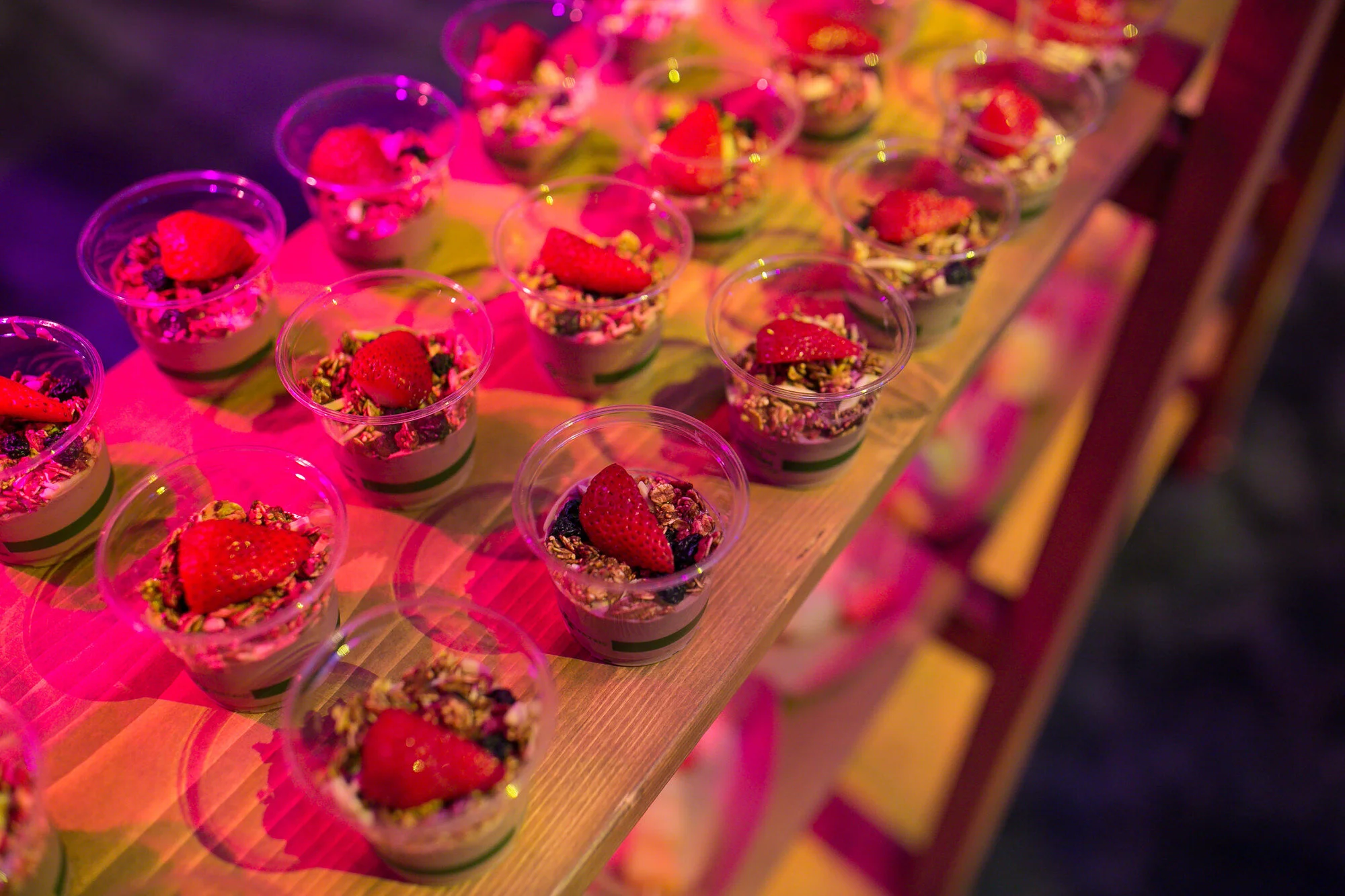  Strawberry desserts arranged in rows are lit in pink lighting 