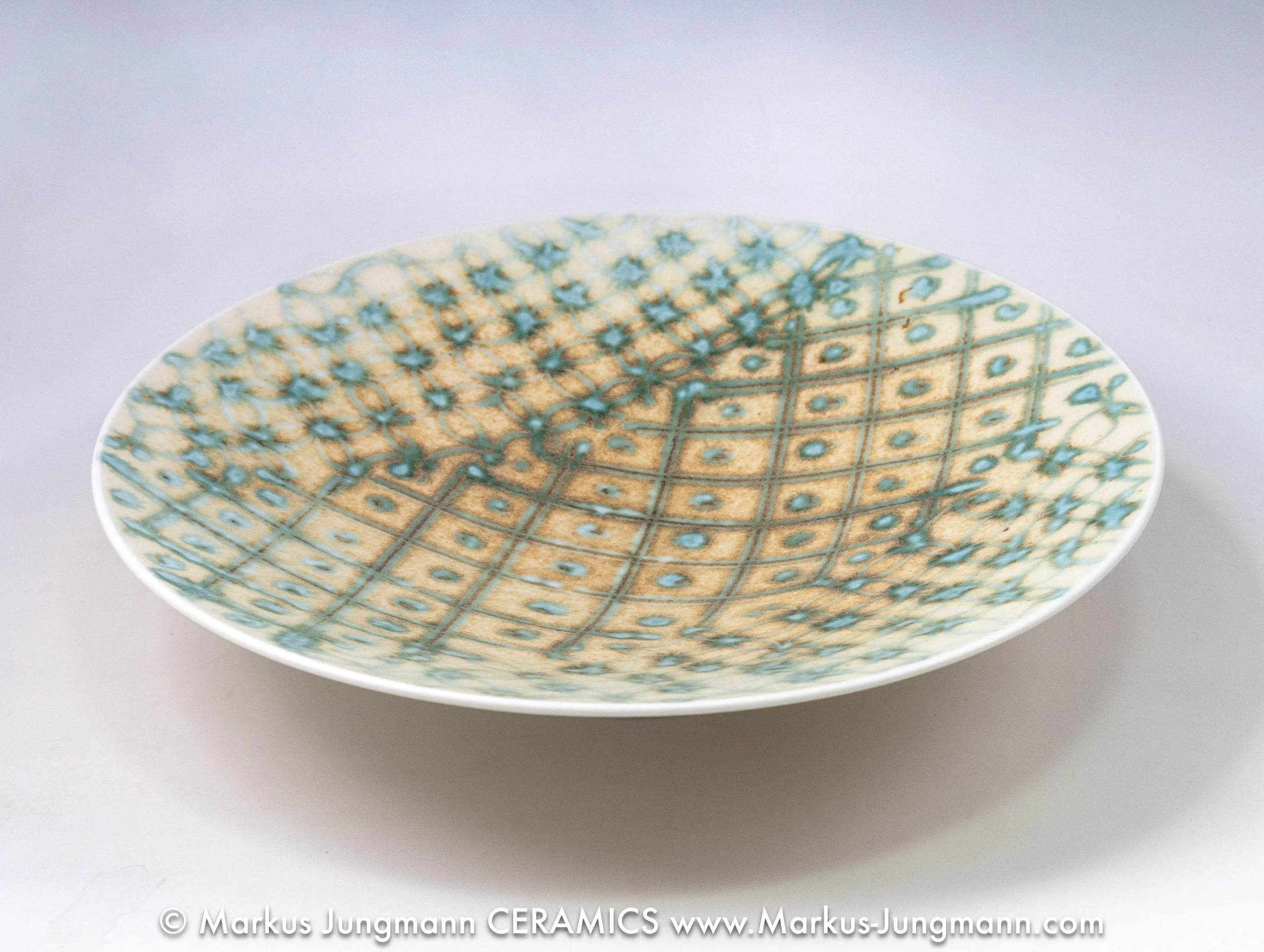 Wheel-thrown porcelain bowl with a teal grid and floral lattice on an oatmeal ground, side view, by Markus Jungmann