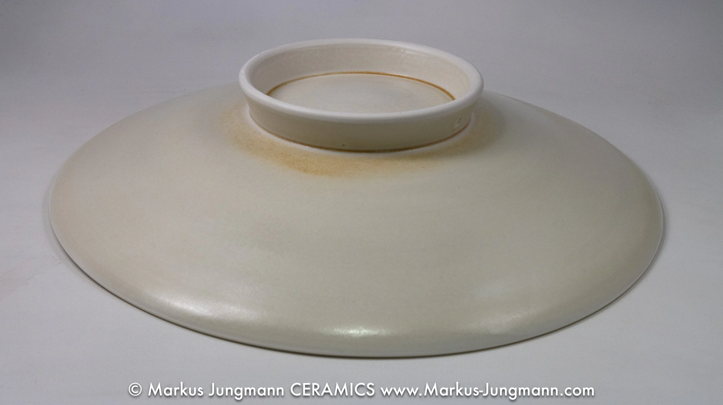 Porcelain bowl with trailed teal lines spiralling from an off-centre point over a warm cream ground, by Markus Jungmann. bottom view