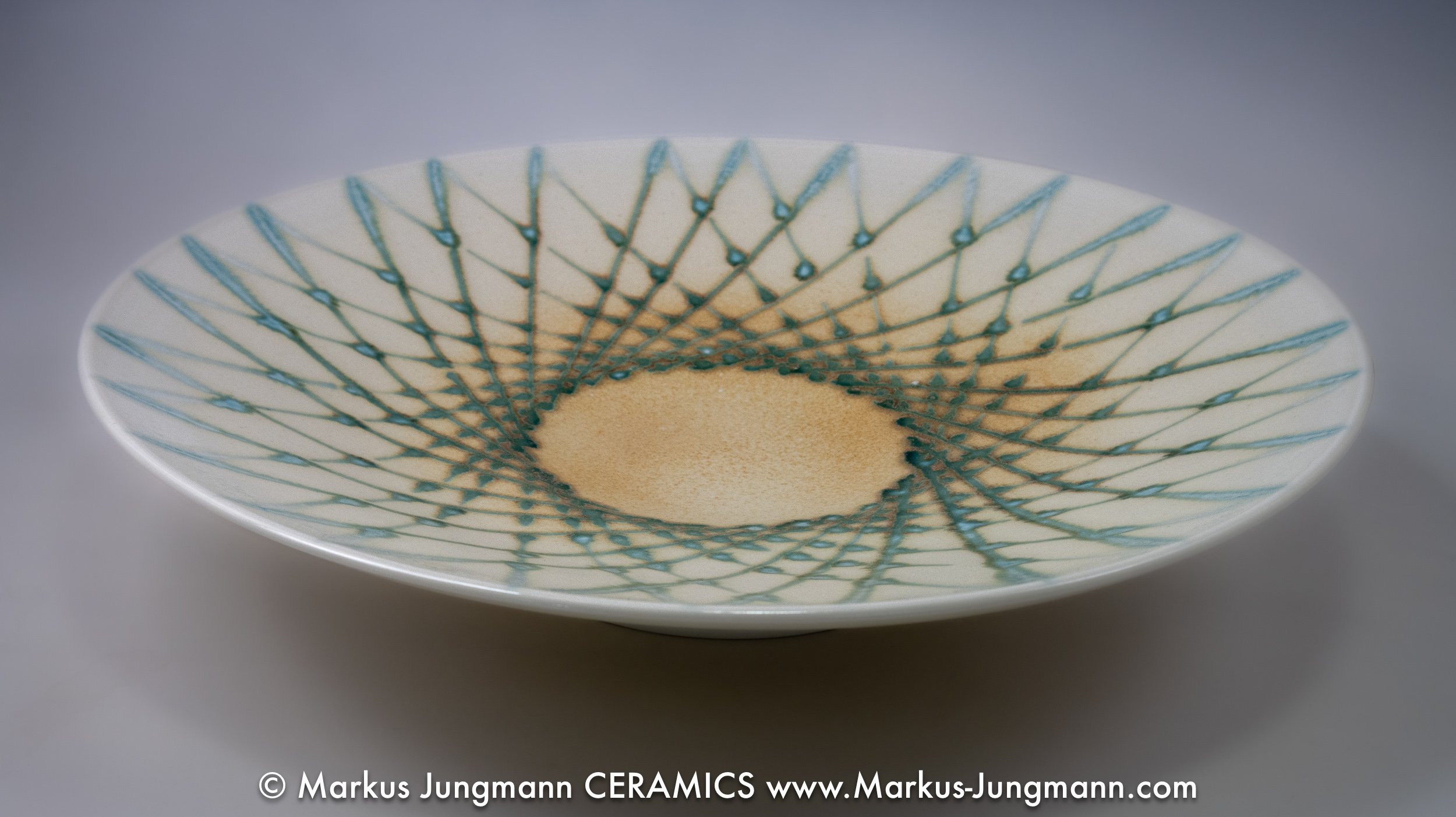 Porcelain bowl with trailed teal lines spiralling from an off-centre point over a warm cream ground, by Markus Jungmann. side view