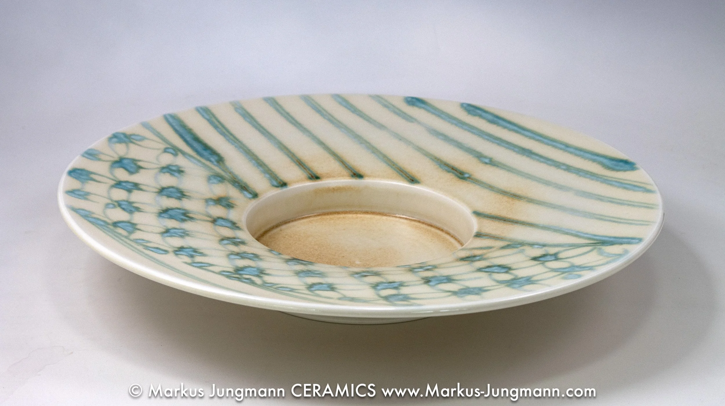 Wide-rimmed porcelain bowl with diagonal teal stripes and an inset net pattern on a cream ground, by Markus Jungmann-side-view