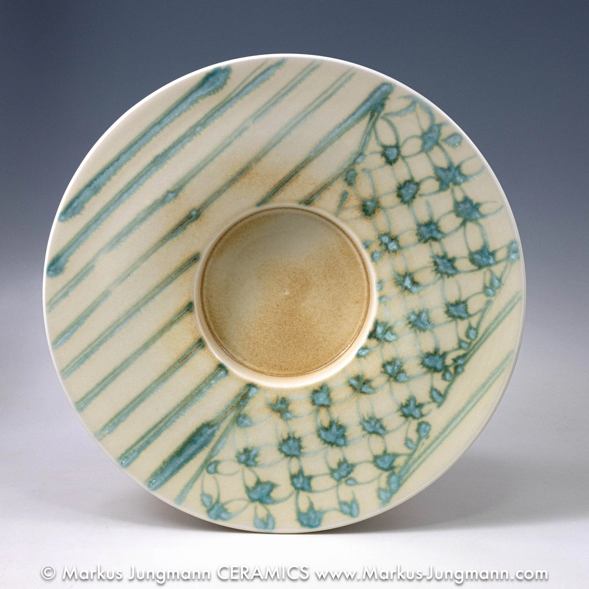 Wide-rimmed porcelain bowl with diagonal teal stripes and an inset net pattern on a cream ground, by Markus Jungmann.